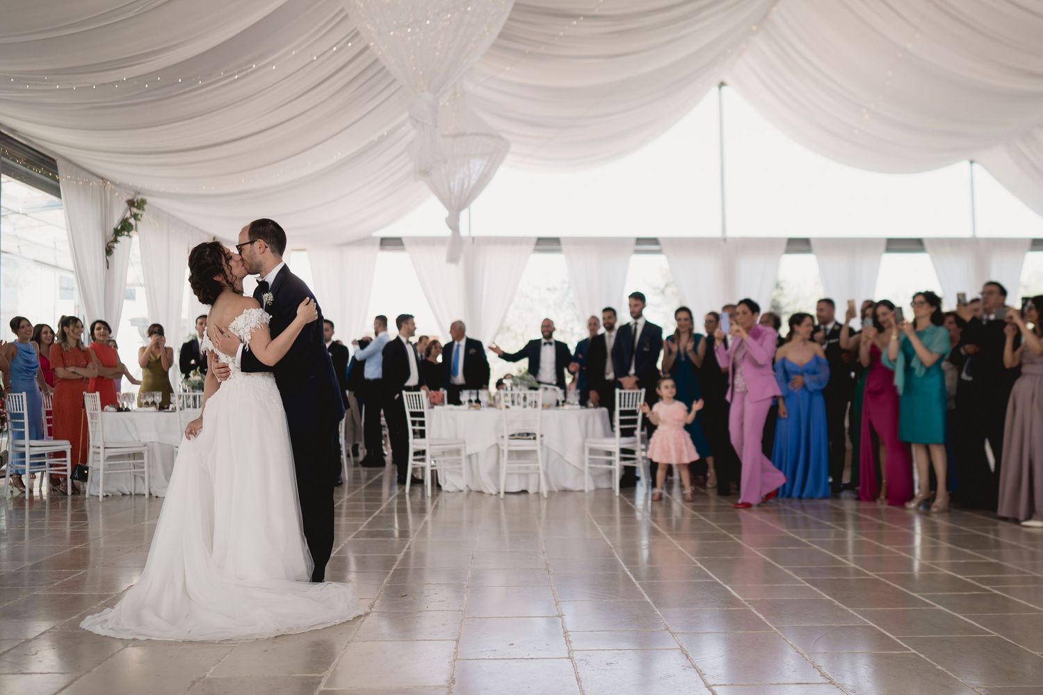 Wedding reception first dance in a white-draped tent with guests watching from tables.
