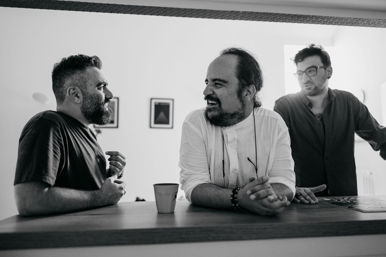Three people conversing at a bar counter in black and white photography.
