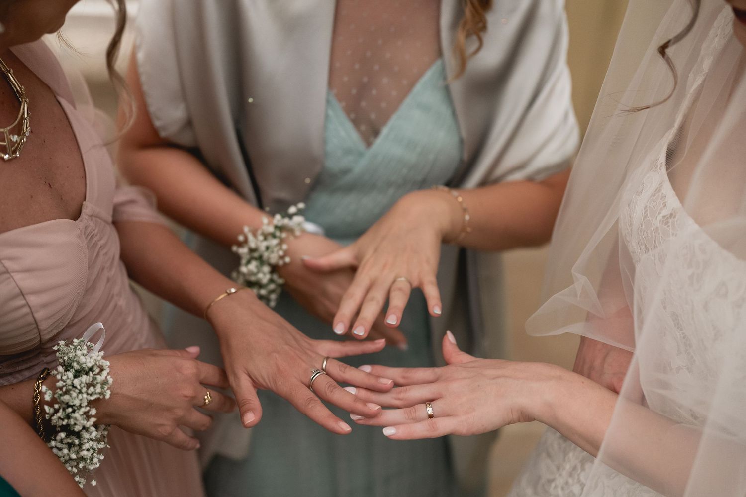 Several hands come together showing wedding jewelry and bridesmaid dresses in soft pastel colors during a bridal celebration.