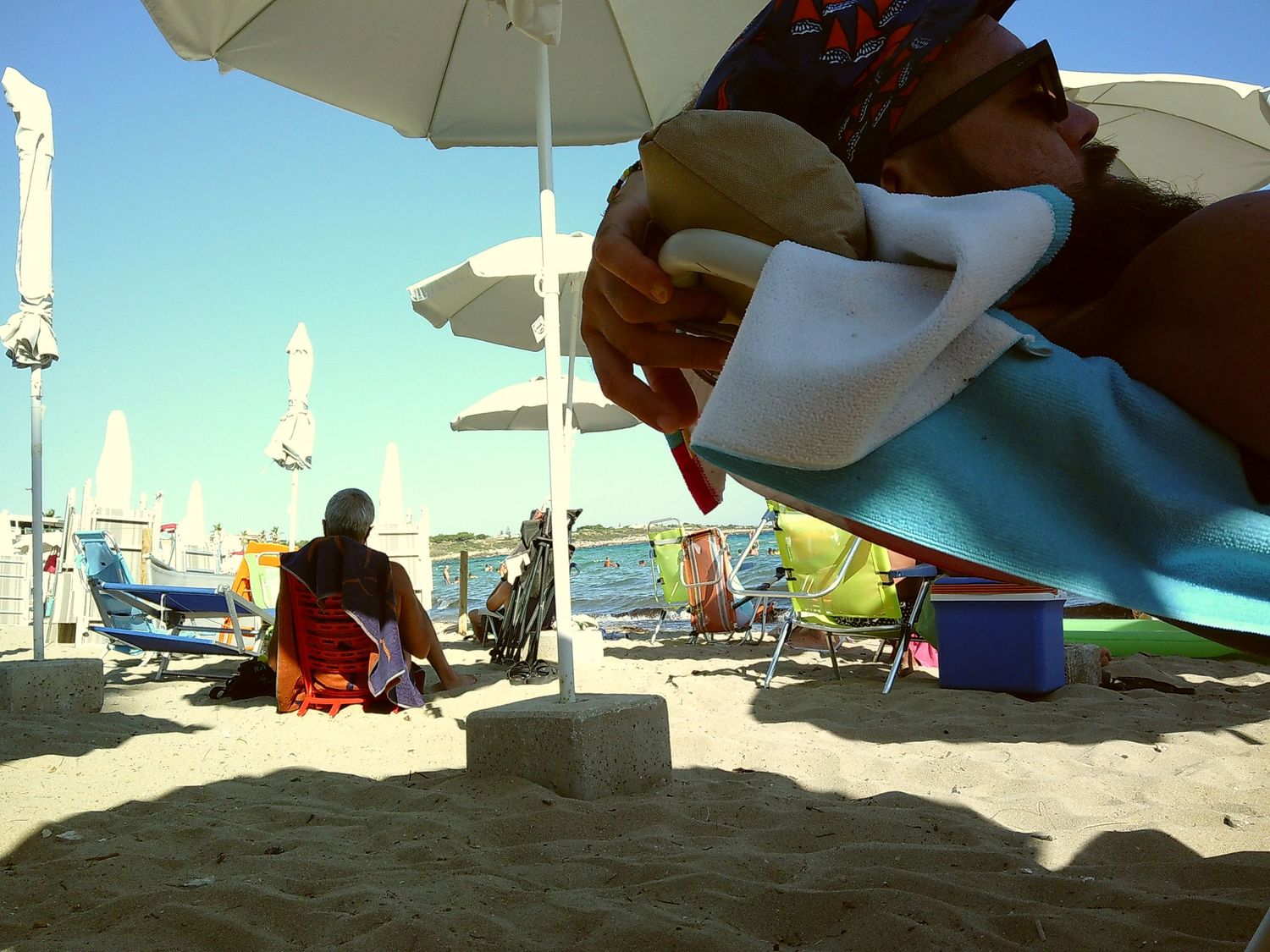 Beach scene with umbrellas and towels casting shadows on golden sand.