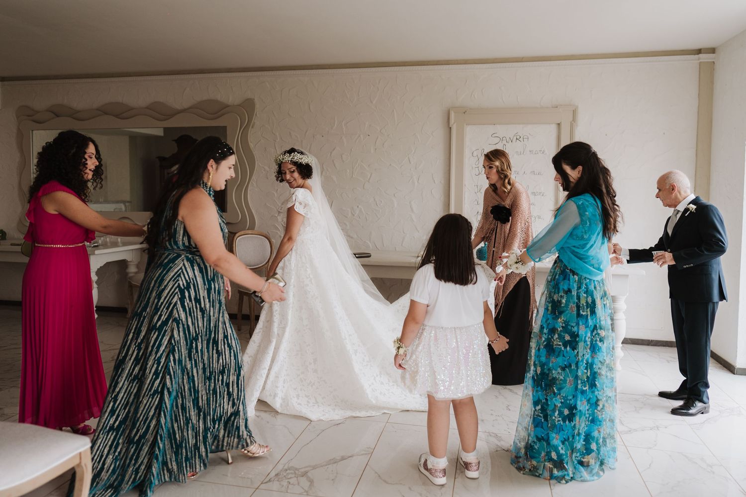 Wedding preparation scene with a group adjusting a long white veil in an elegant room.