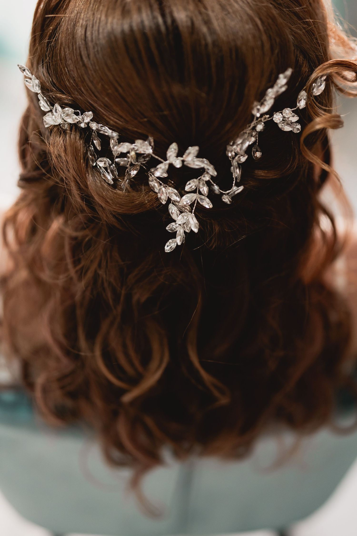 Close-up of delicate crystal floral hair accessory adorning wavy brown hair in an elegant bridal style.
