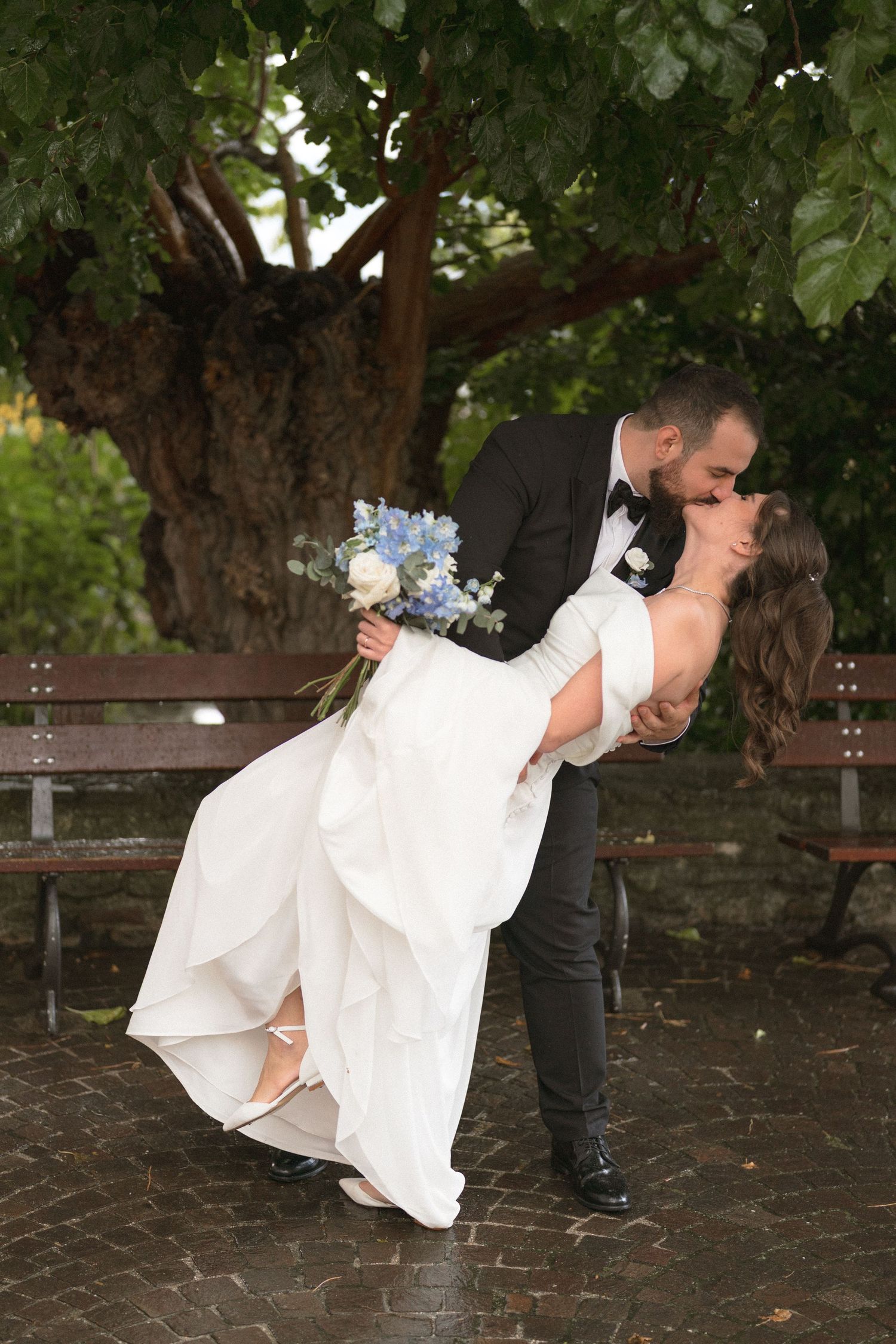 Romantic dip pose between newlyweds under trees in formal attire.