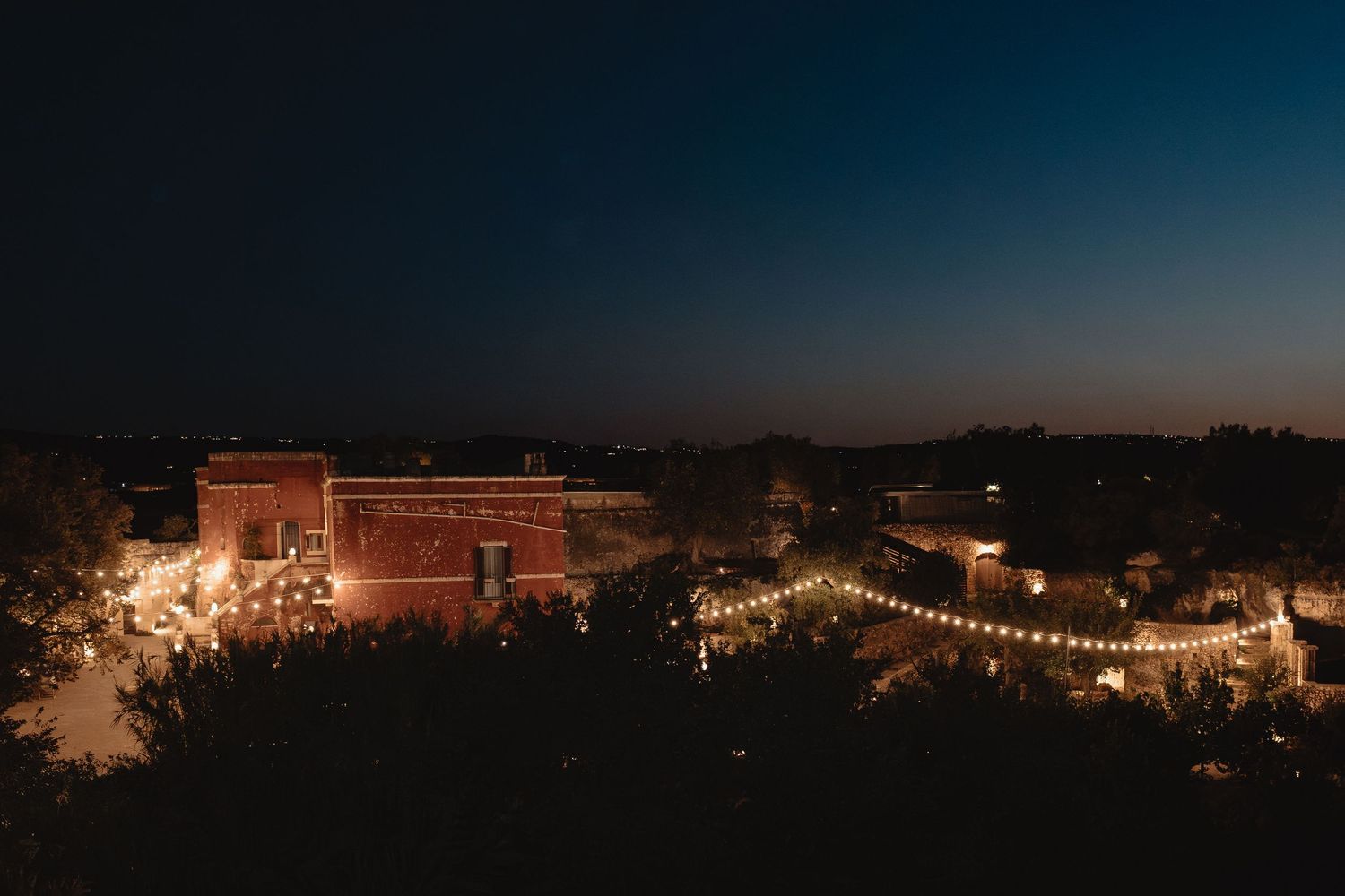 Panoramic nighttime view of illuminated buildings and string lights against a dark sky.