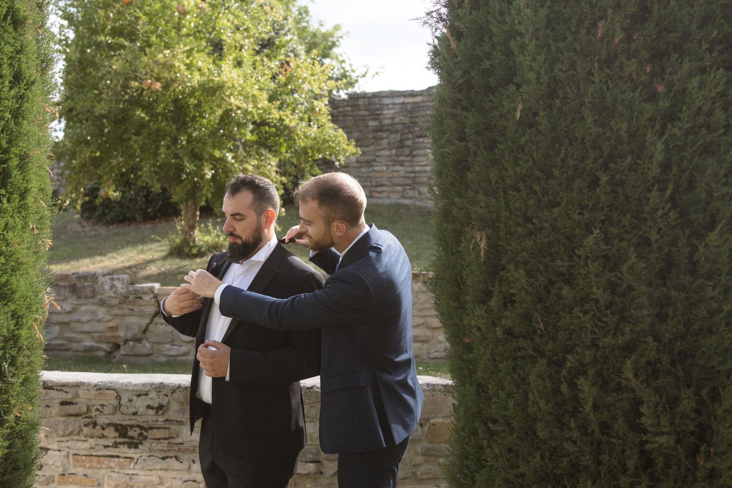 Wedding guests gathered in a garden setting among cypress trees and stone walls.