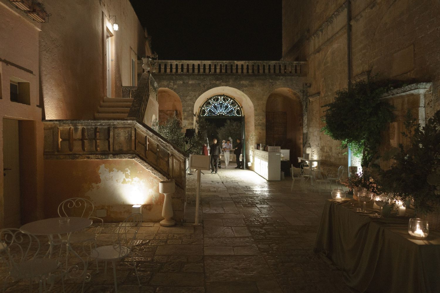 Stone courtyard and archway illuminated by warm lighting and candles creating a romantic evening atmosphere.