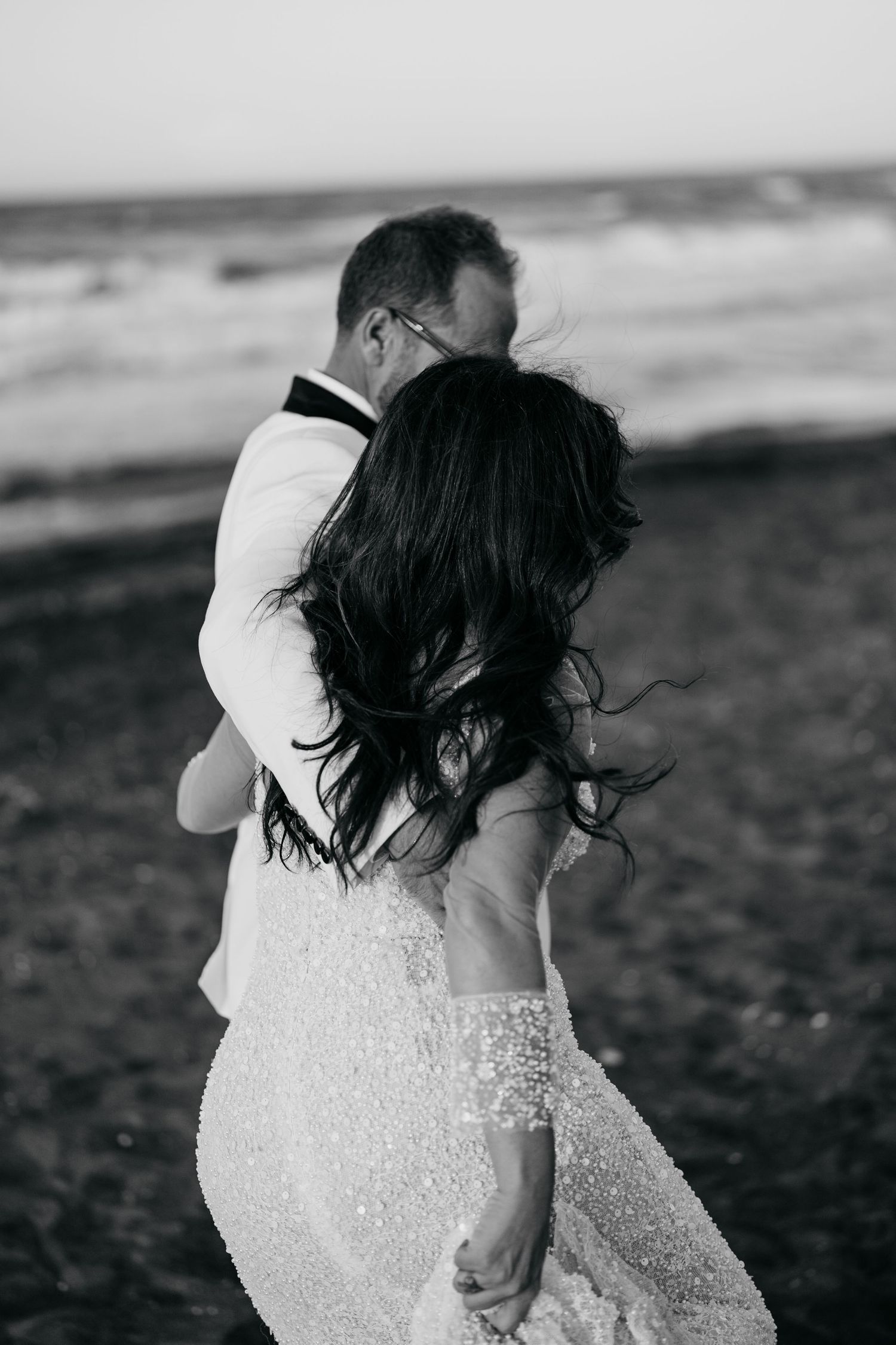 Romantic black and white portrait of couple embracing on windy beach.