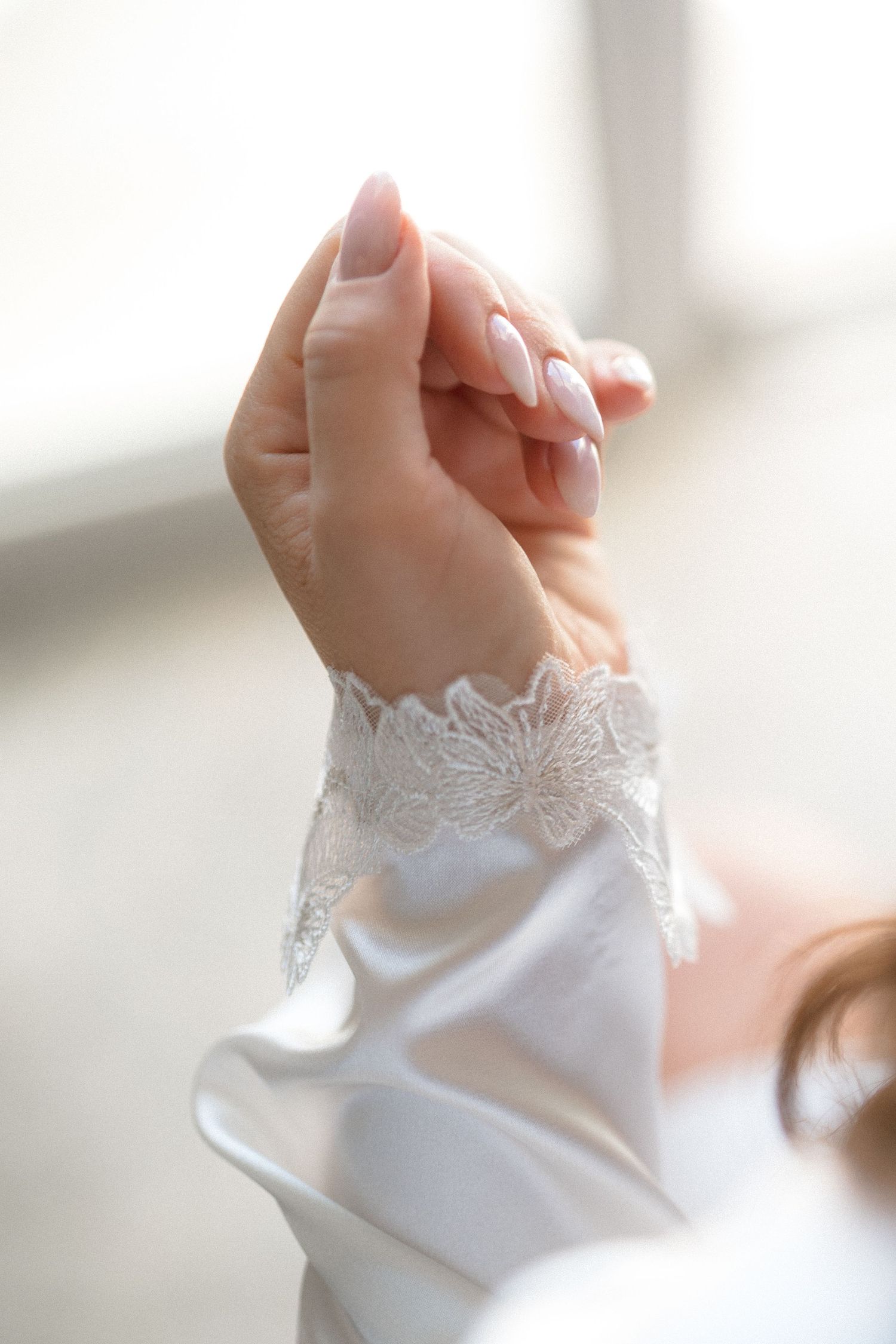 Close-up of an elegant white lace sleeve detail on a bridal gown with delicate hand pose.
