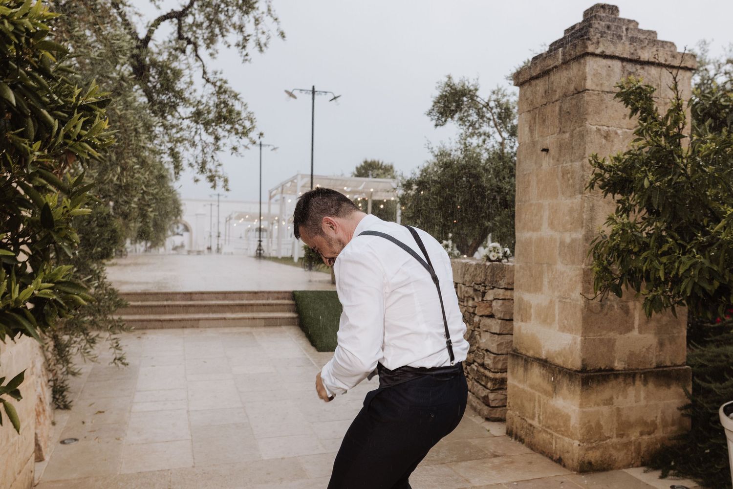 A person in formal attire peeks around a stone pillar outdoors.