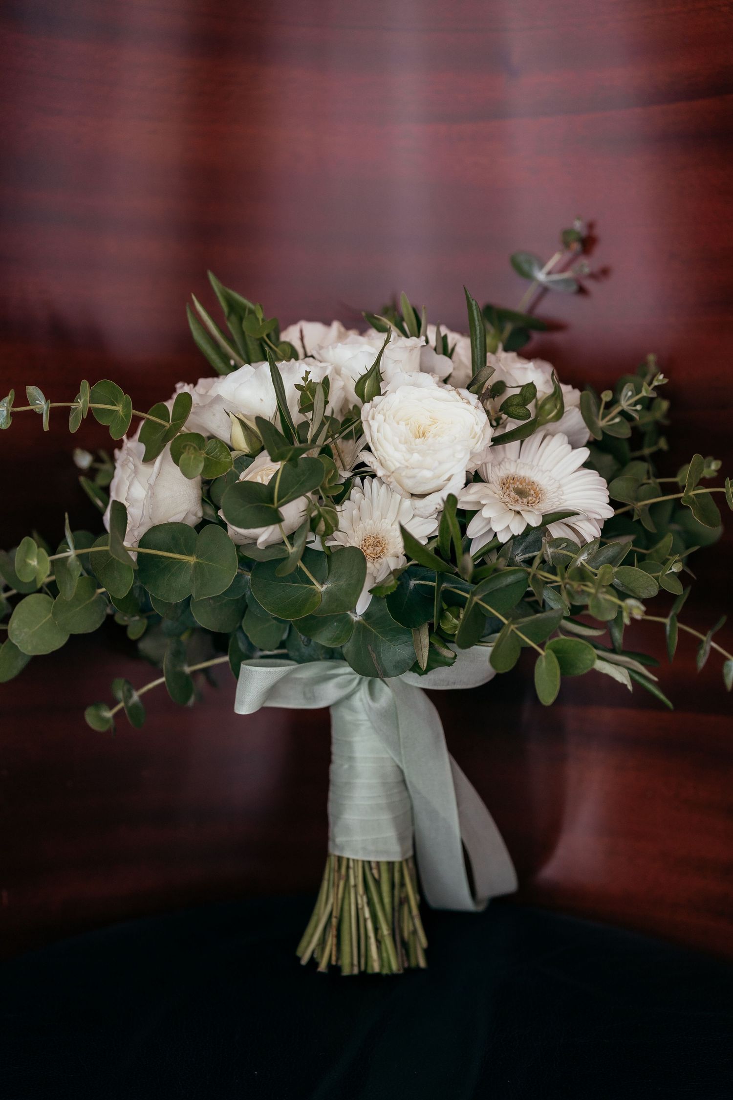 Elegant white wedding bouquet with roses and eucalyptus wrapped in ribbon.