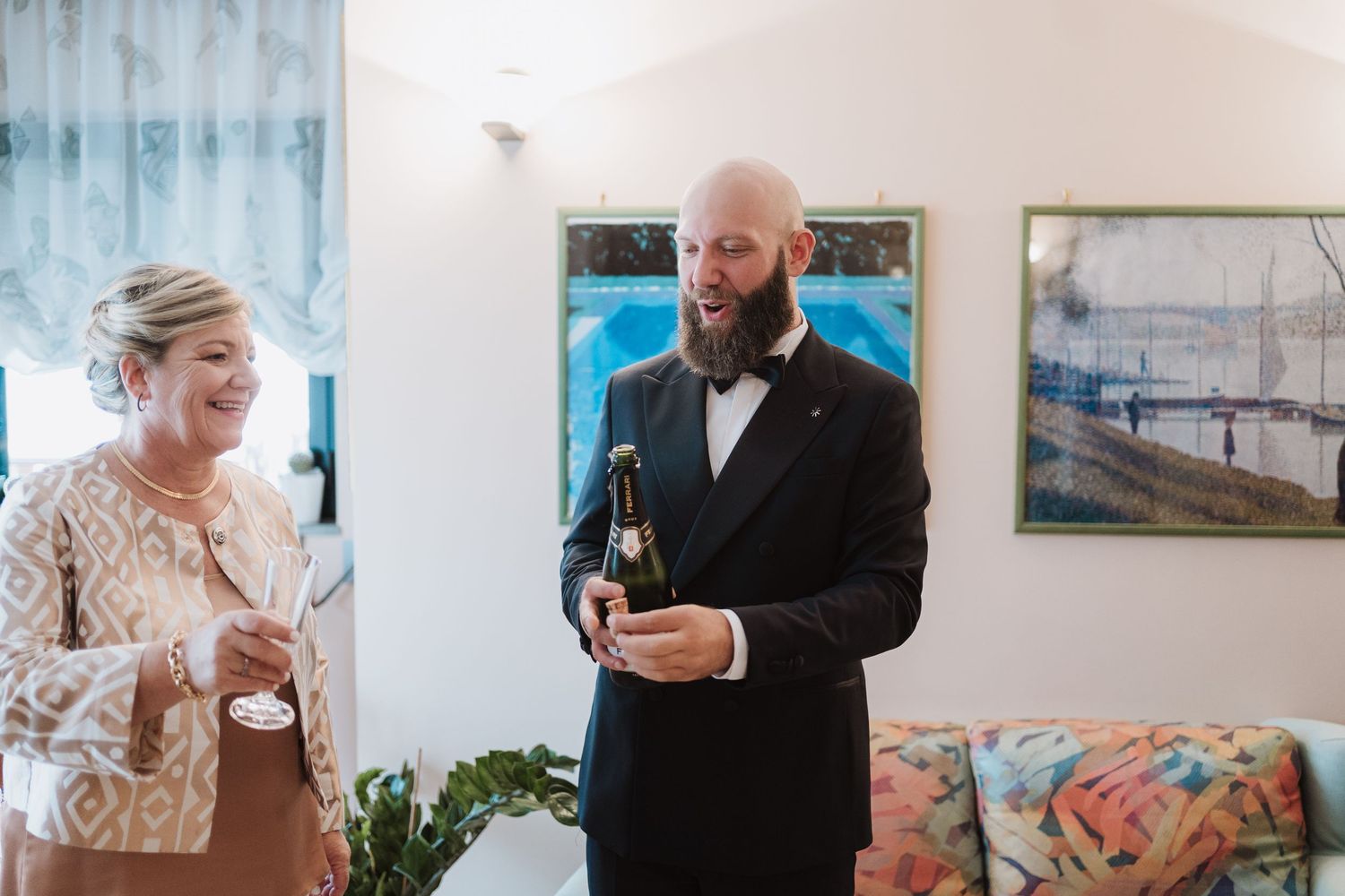A couple celebrates their wedding day by opening a champagne bottle in an elegant indoor setting.