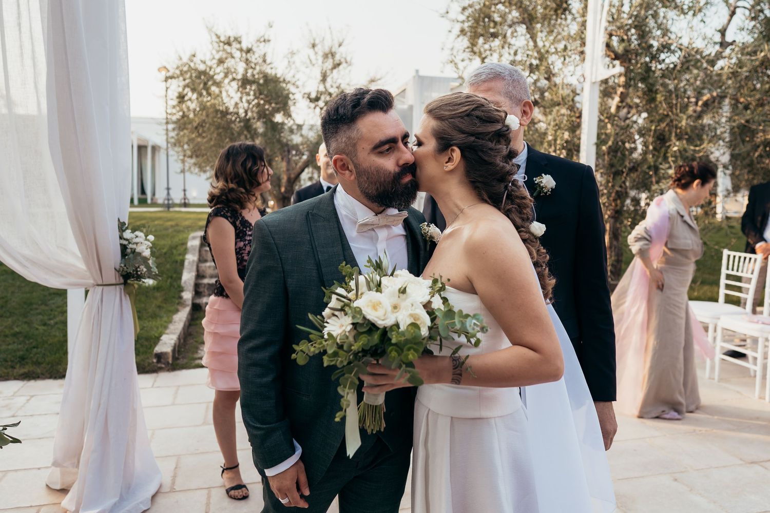 Intimate wedding moment captured with white floral bouquet and outdoor setting.