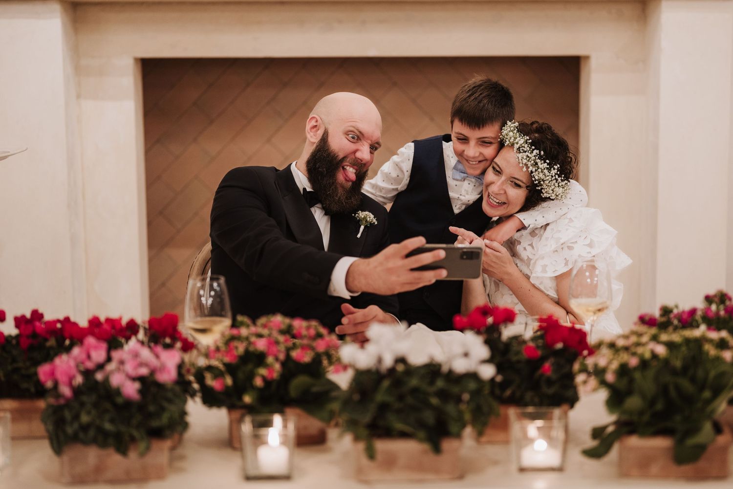 Three wedding guests share a candid moment at a floral-decorated reception table.