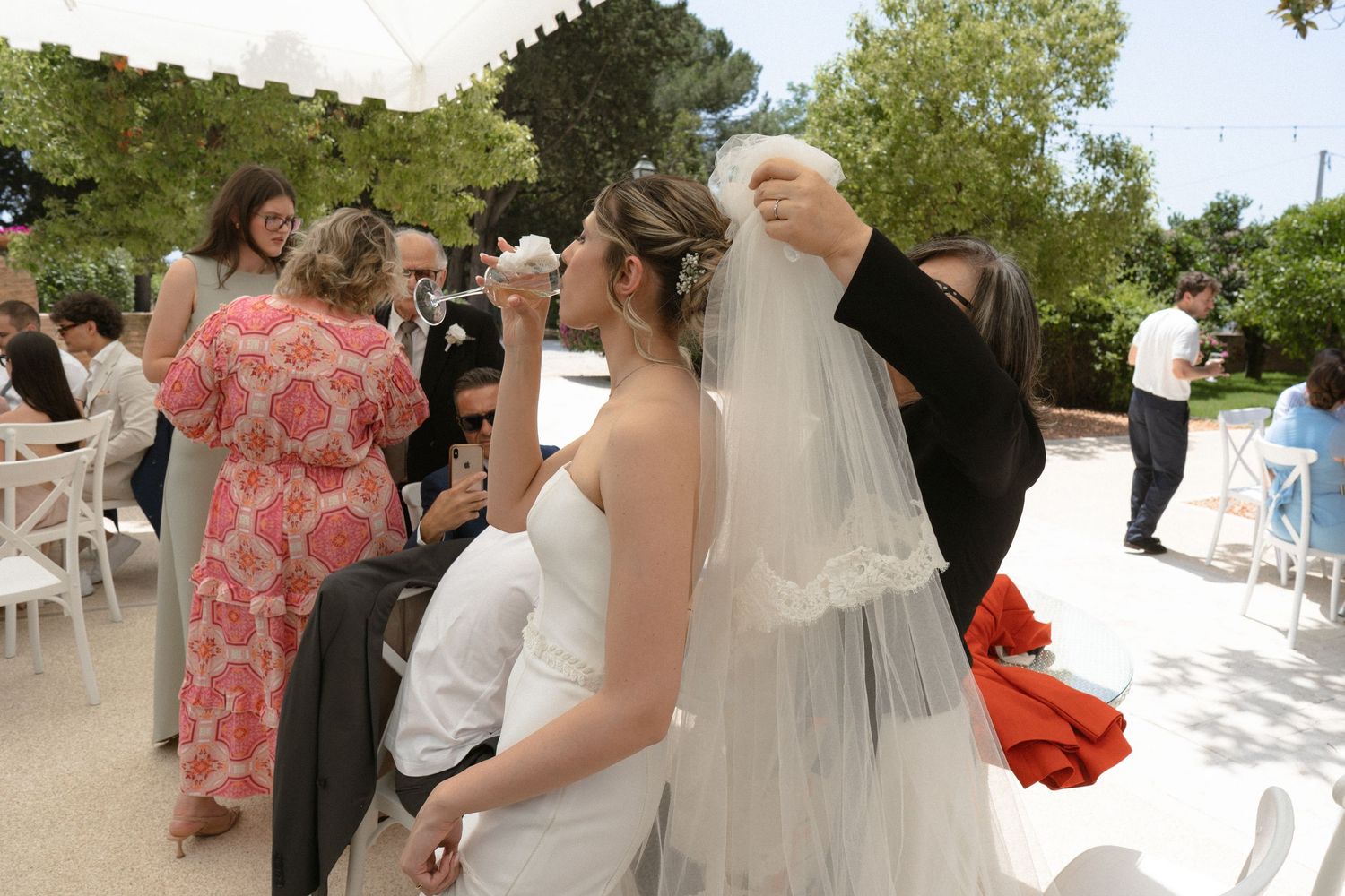 Wedding guests gather outdoors on a sunny day for a celebration at an elegant venue.