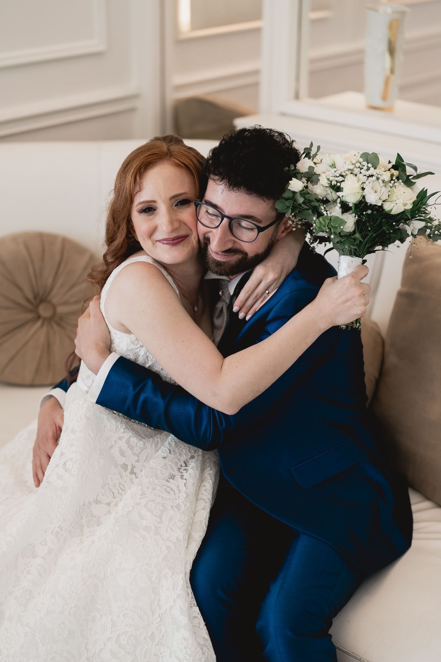 Newlyweds share a tender embrace in a beautifully decorated room with white flowers and elegant decor.