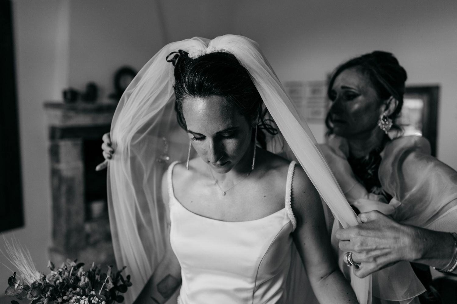 A black and white photo capturing final wedding preparations as a veil is being adjusted.