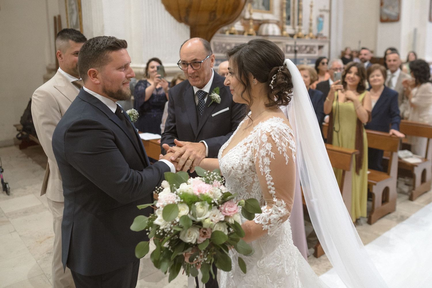 A wedding ceremony takes place inside a traditional church with guests watching from wooden pews.