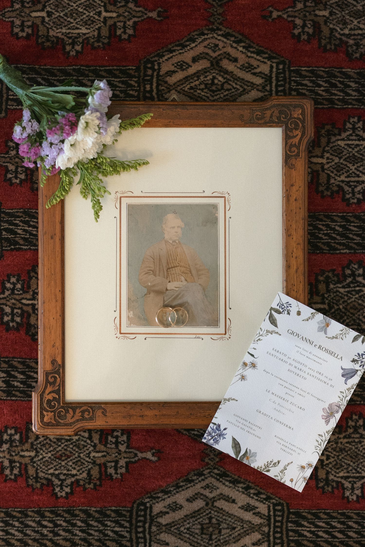 Vintage framed photograph on ornate rug with purple flowers and invitation card displaying elegant design details.