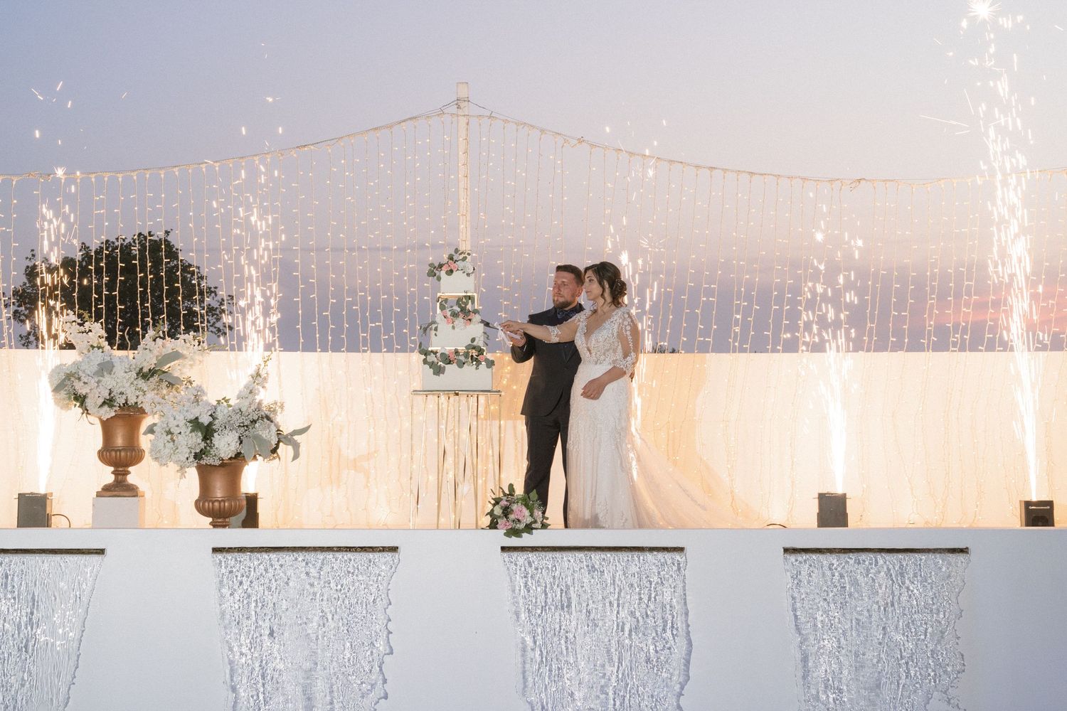 Wedding reception venue decorated with sparkling lights and floral arrangements at sunset.