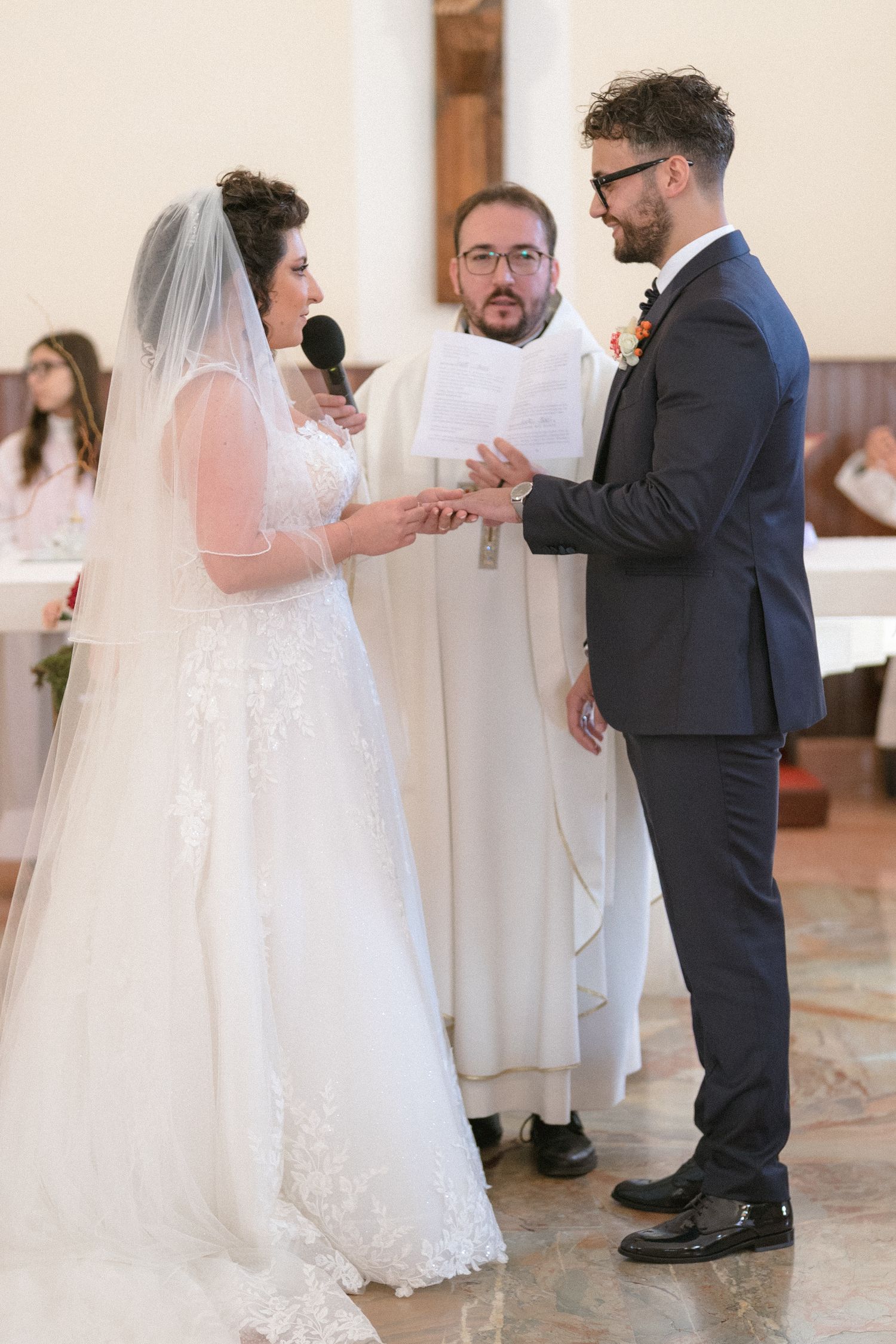 Bride places wedding ring on groom's finger before priest during church ceremony.