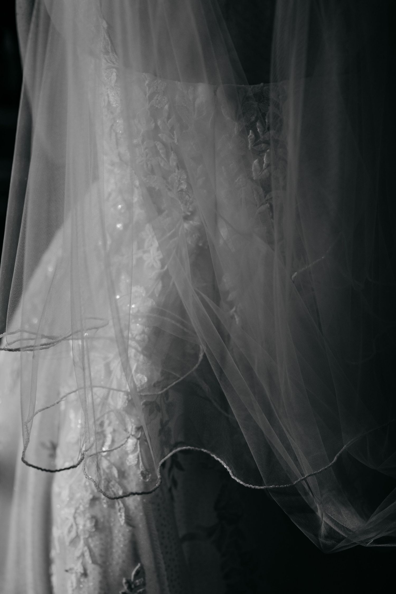 Close-up black and white detail of delicate lace wedding dress and flowing bridal veil.