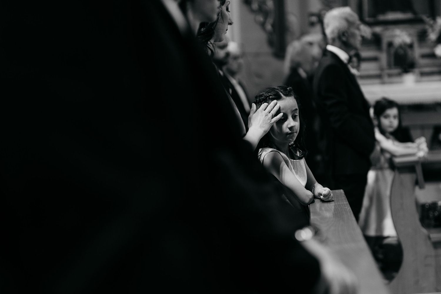 Black and white candid photograph of wedding guests during ceremony.