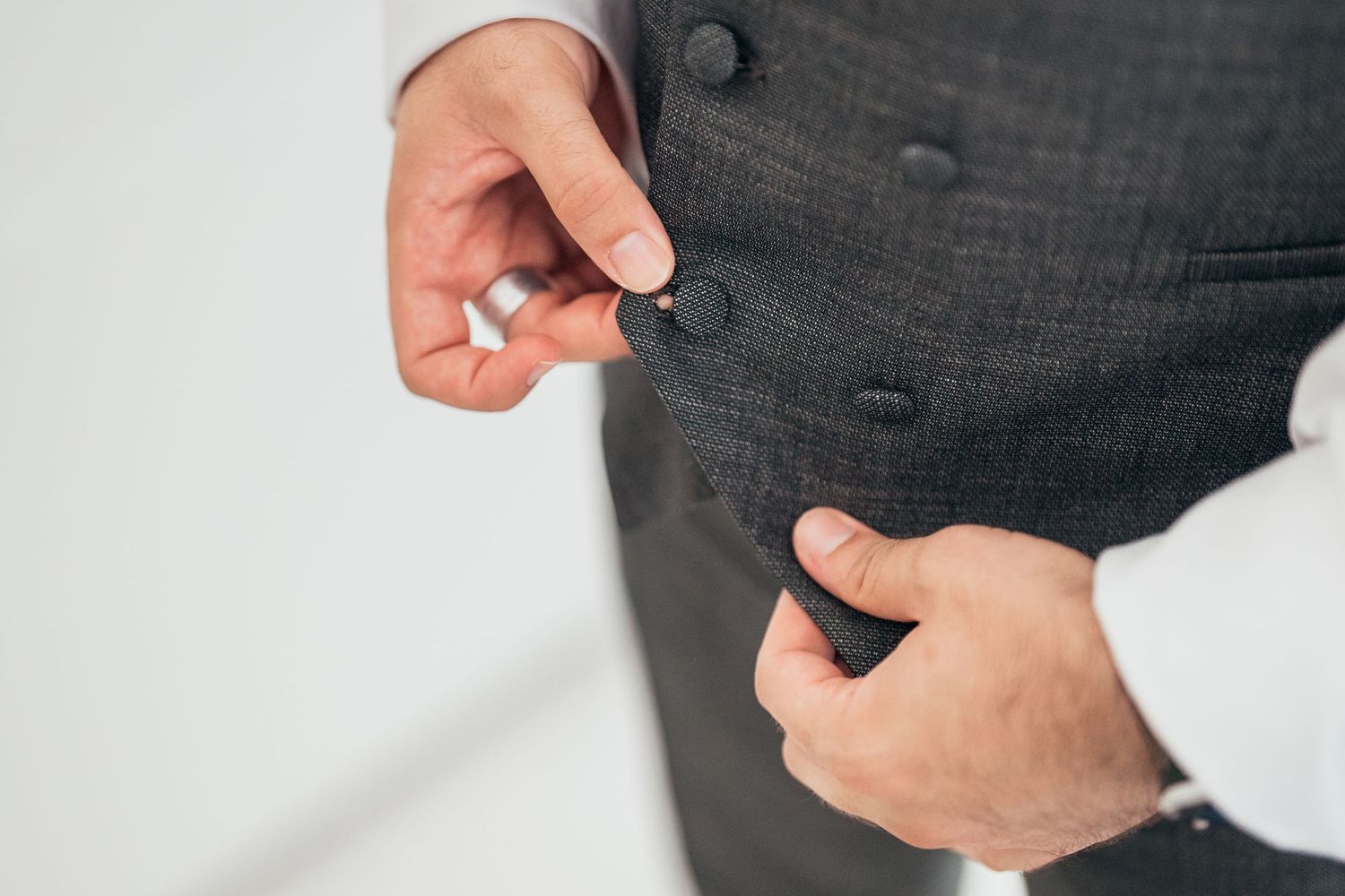 Close-up of hands fastening buttons on dark formal attire.