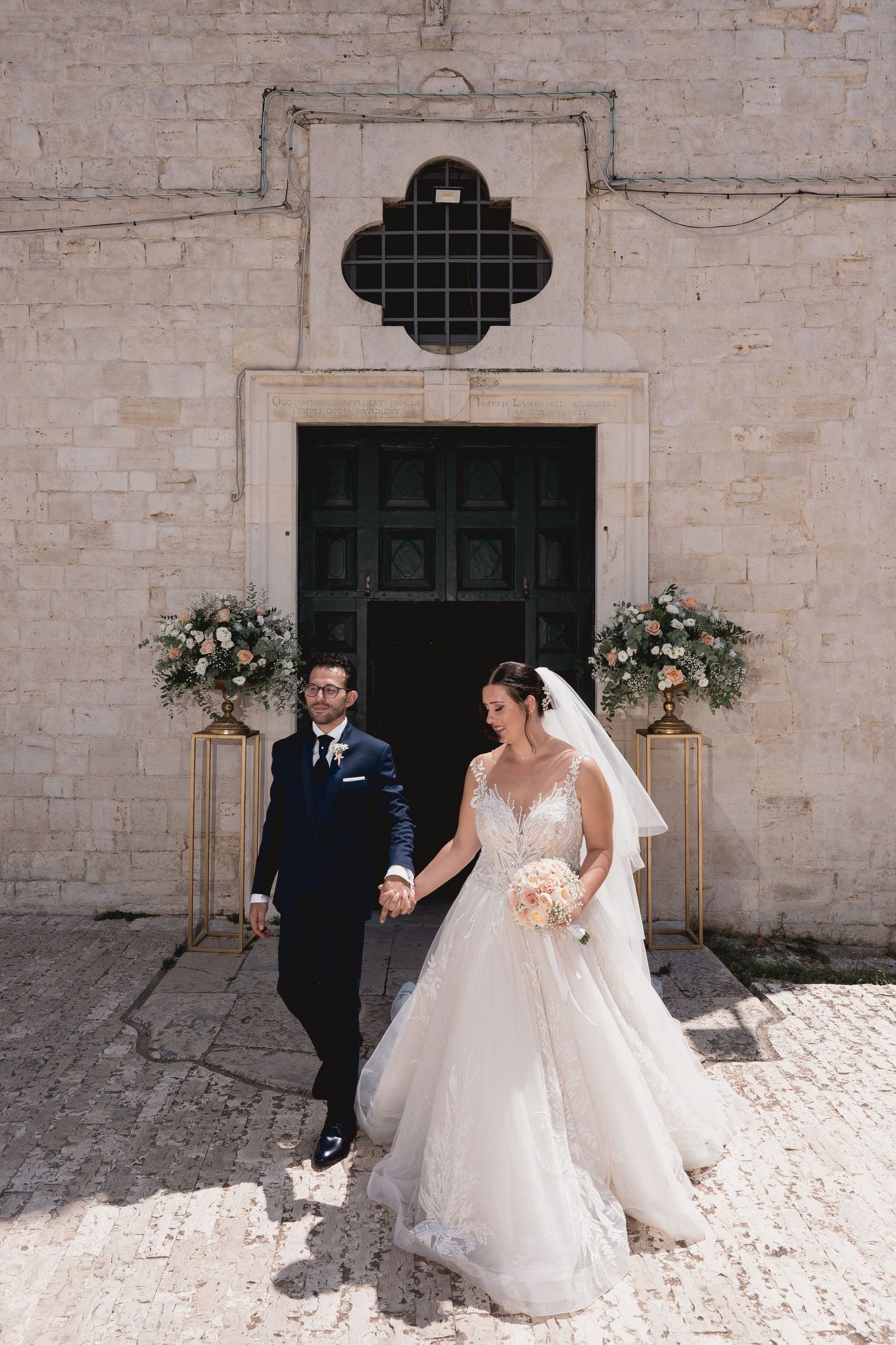 A couple pose in front of a rustic church door adorned with floral arrangements.