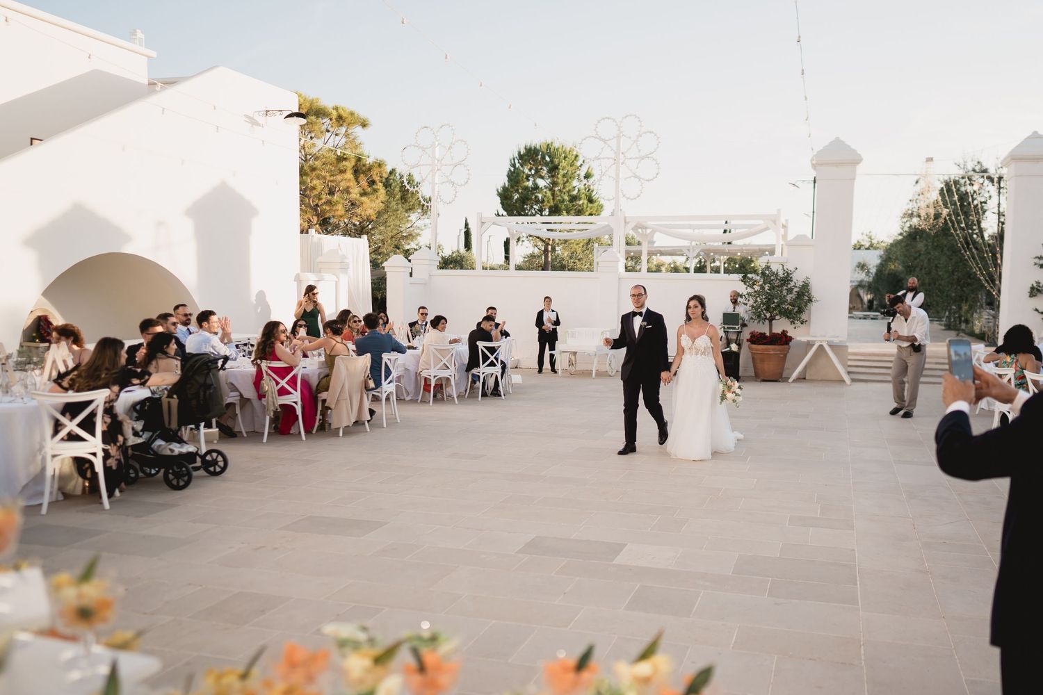 An elegant outdoor wedding reception on a white terrace at sunset.