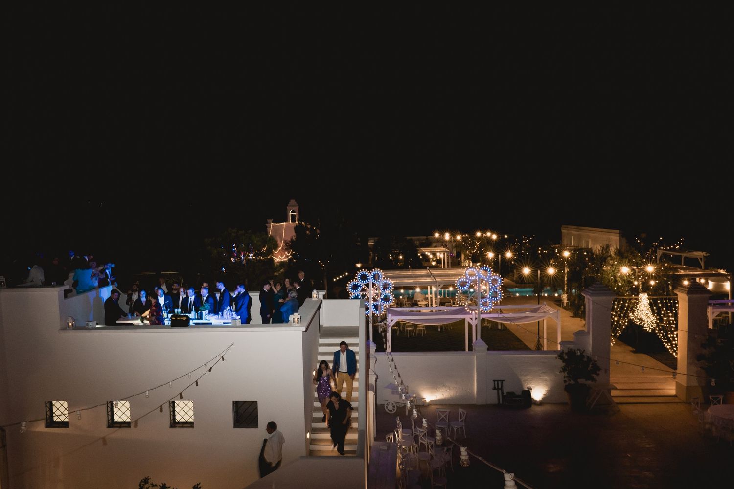 Nighttime rooftop wedding reception with blue lighting and string lights illuminating the venue.