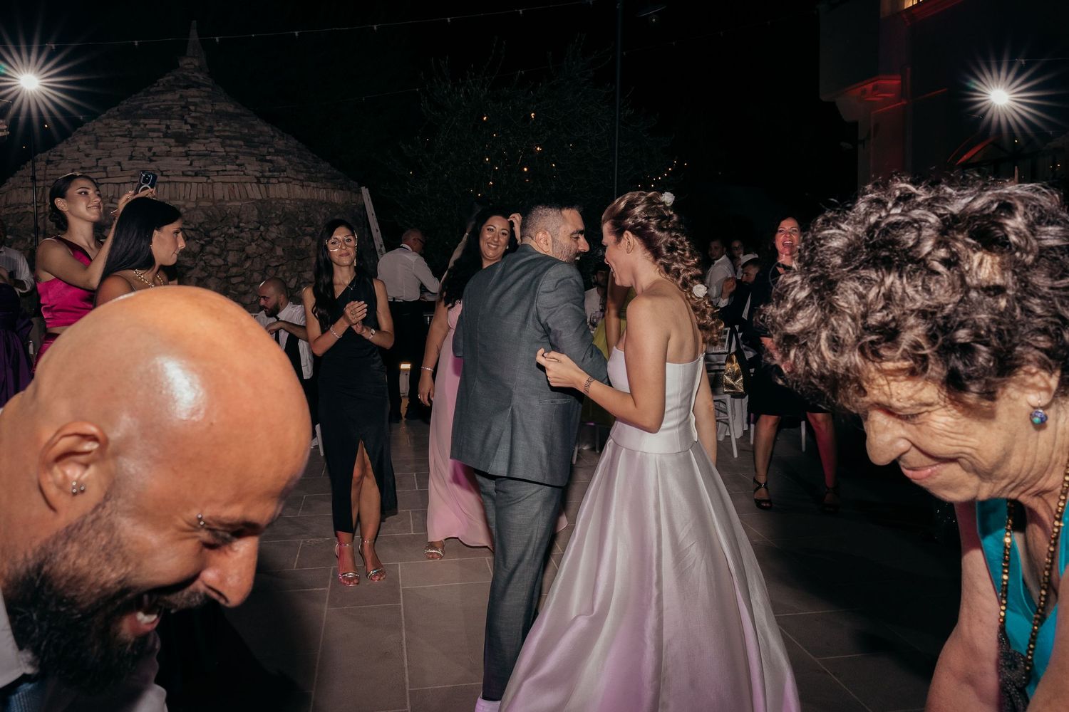 Wedding guests dancing and celebrating during a reception with dramatic lighting.