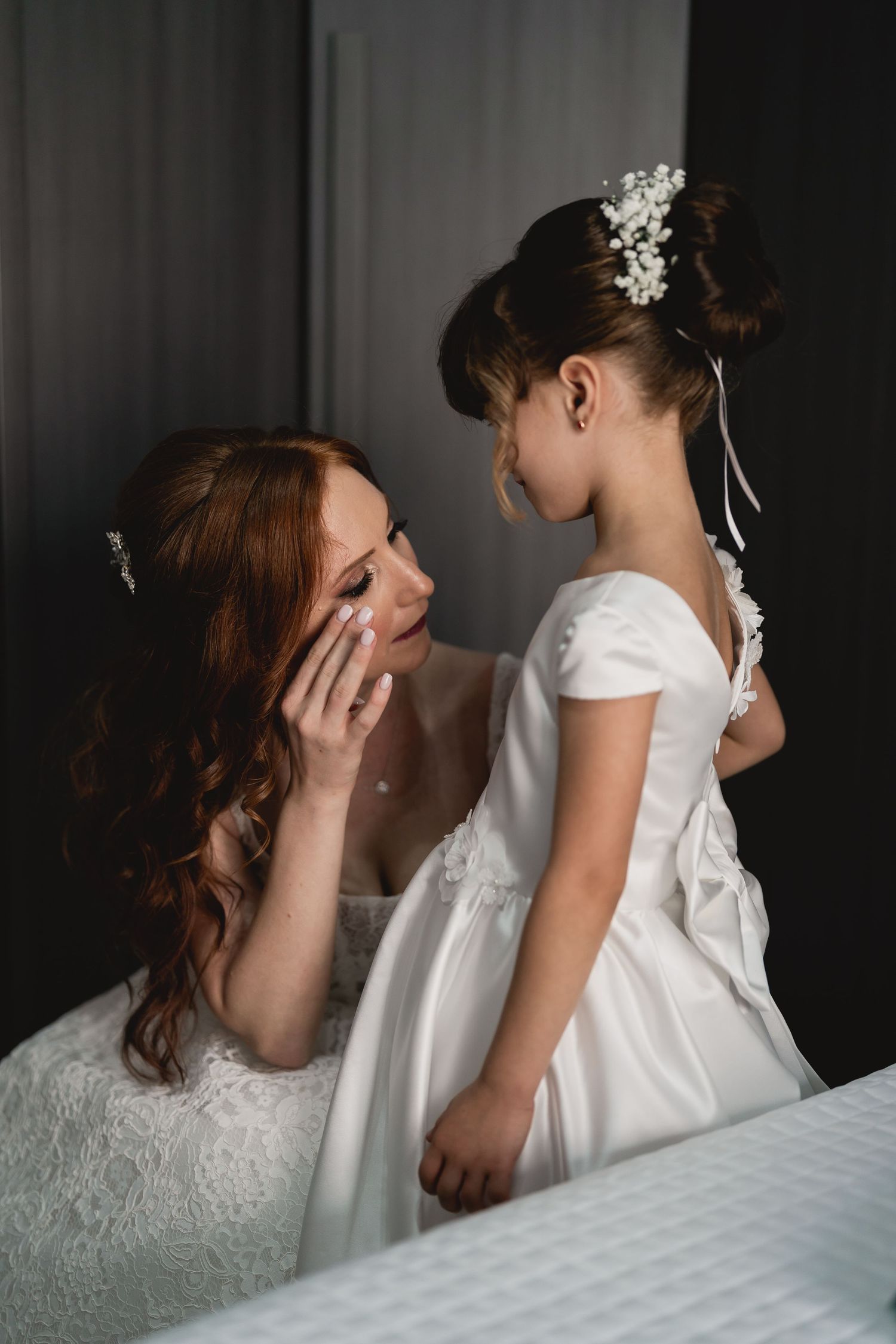 A tender moment between a bride and young attendant both wearing white dresses.
