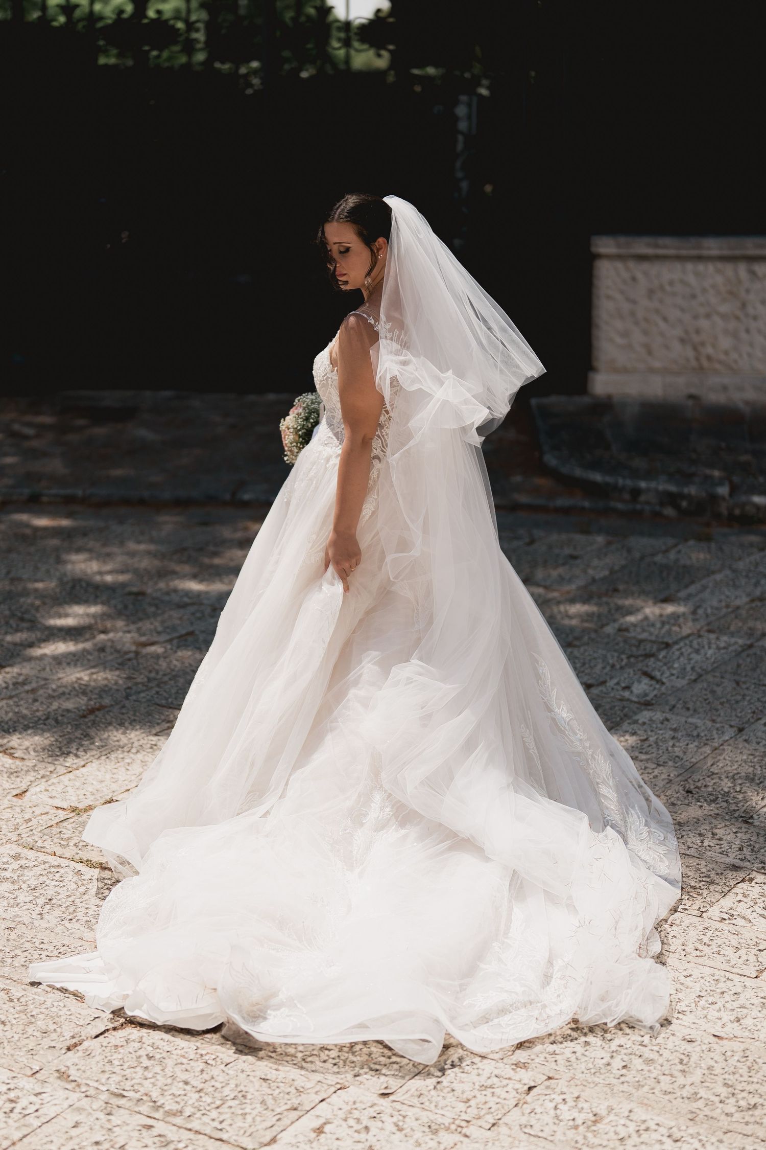 Elegant wedding dress with flowing train and veil photographed outdoors.