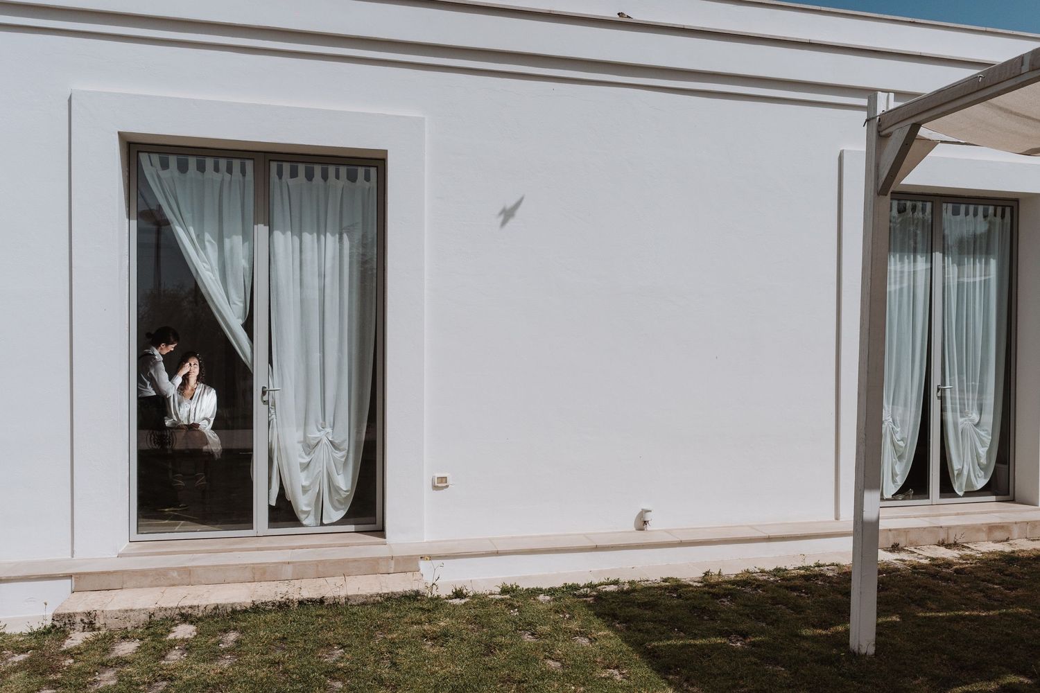 White curtains frame a window in a modern white building exterior.