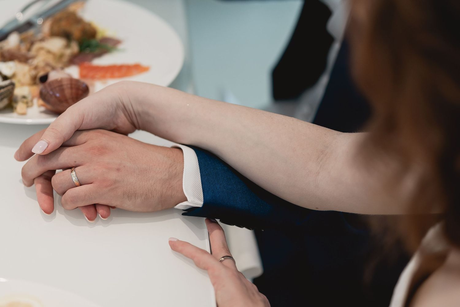 Close-up of couple's hands with wedding rings at a reception table.