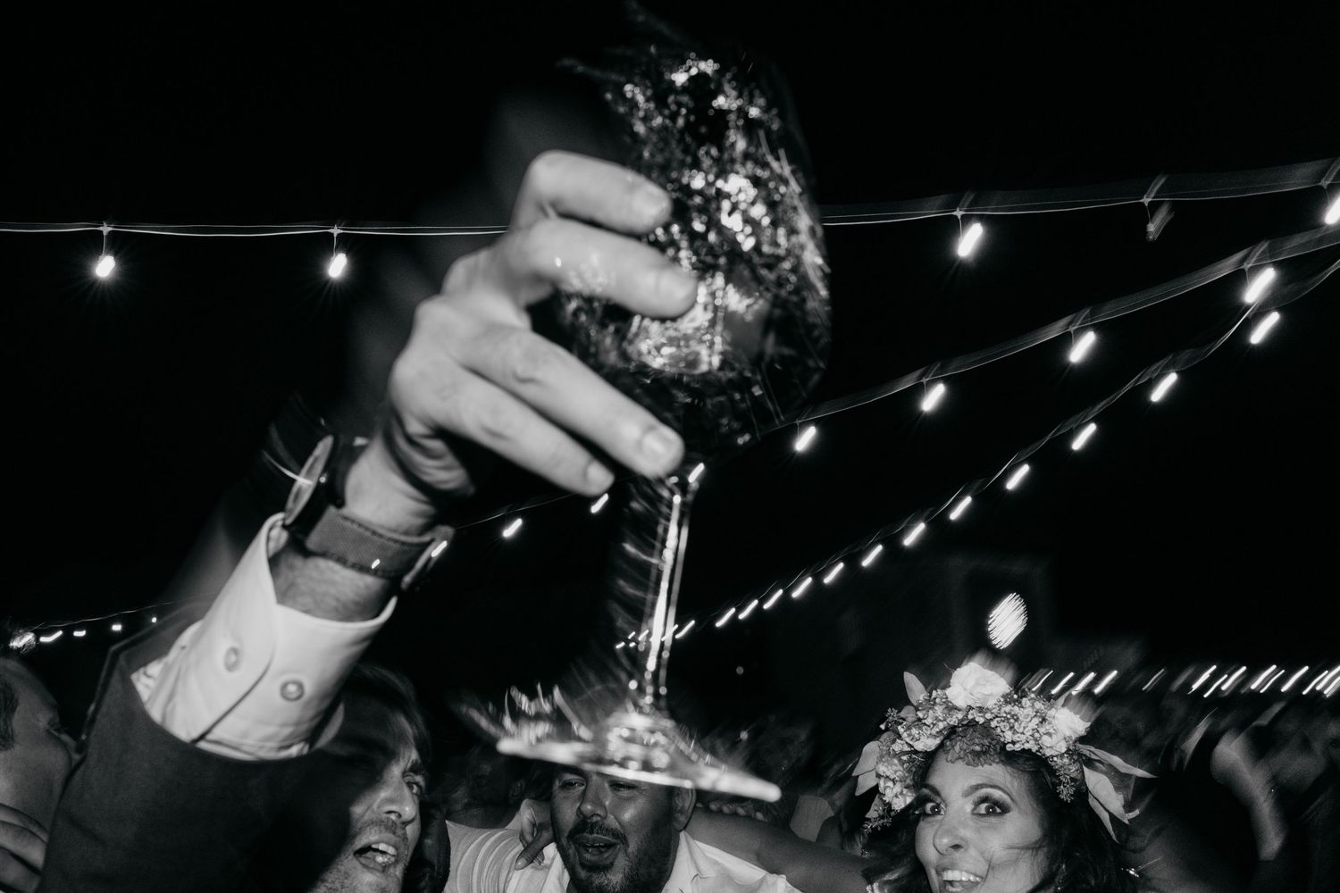 Black and white photos of a wedding celebration with dancing and champagne toasts under string lights at night.
