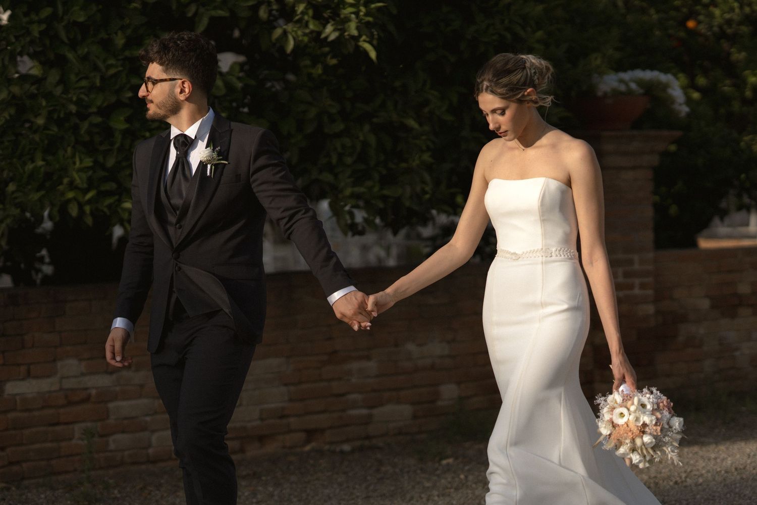 Wedding couple poses in formal attire against a lush garden setting.