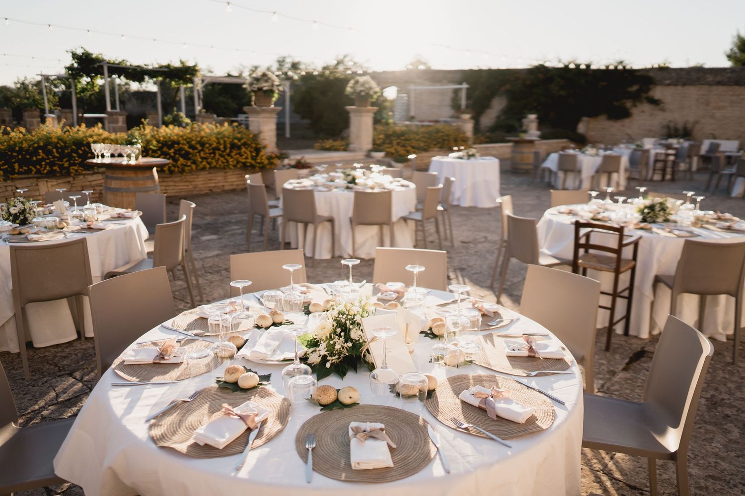 Elegant outdoor wedding reception setup with round tables dressed in white linens and floral centerpieces.