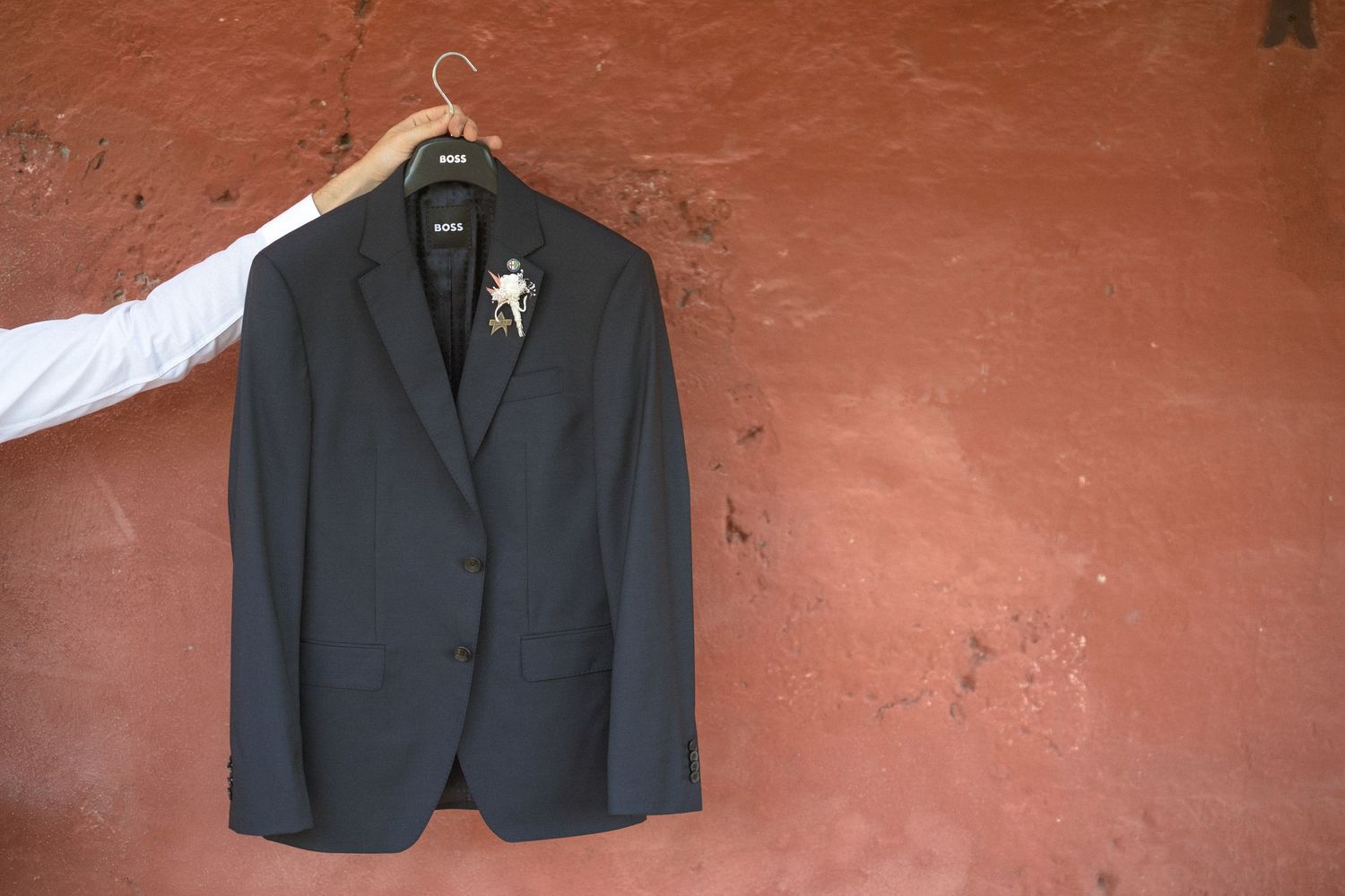 Black formal suit jacket hanging against a terracotta colored wall.