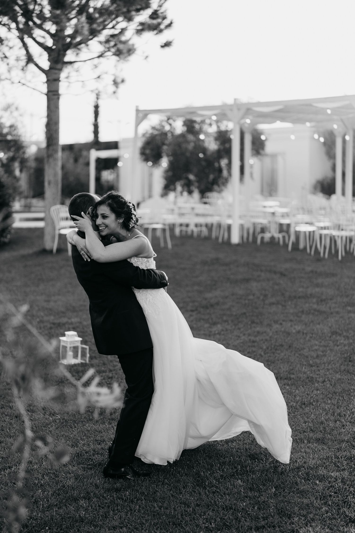 Couple in wedding attire dancing and spinning on a grassy lawn at dusk.