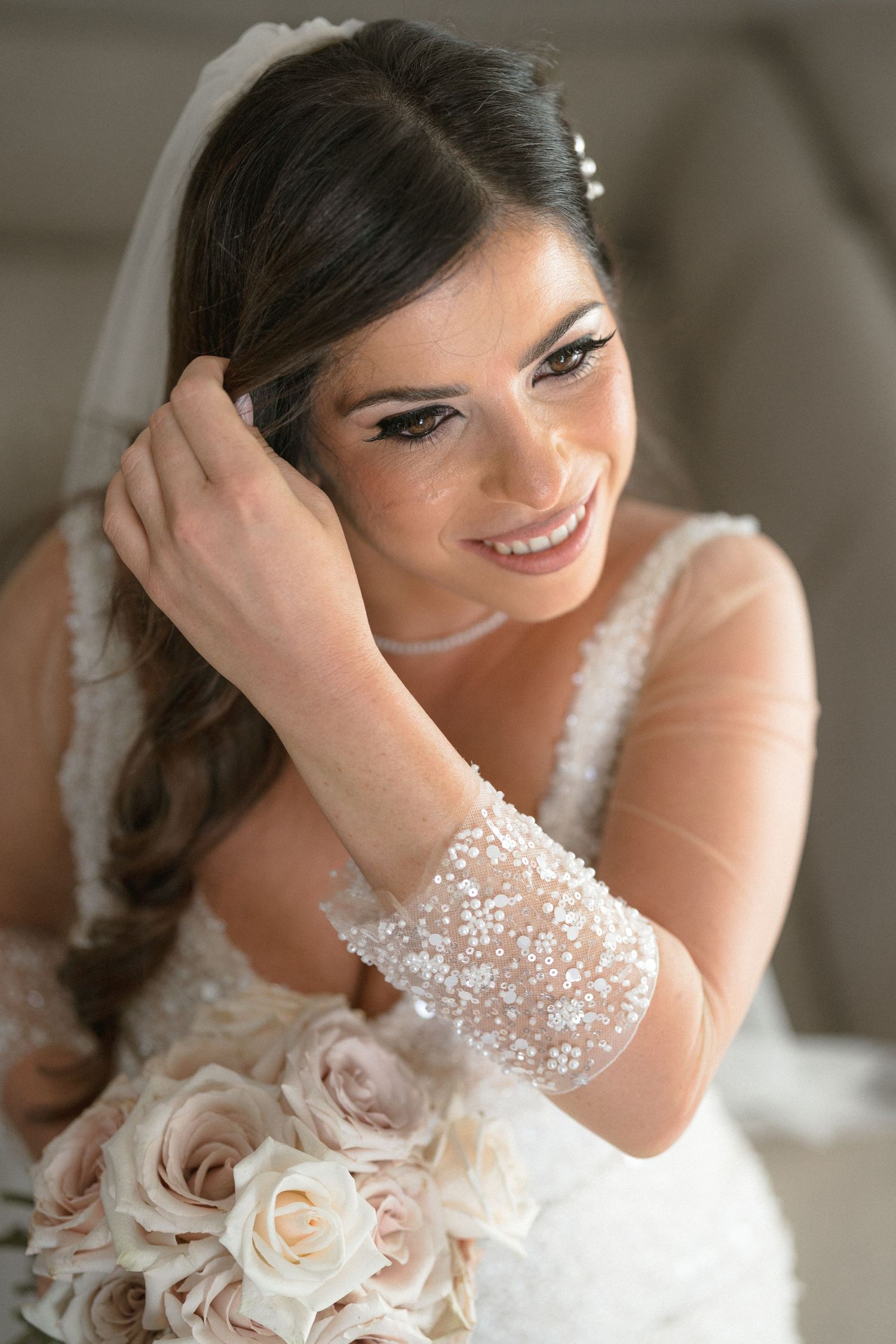 A bride in a white lace dress holds a bouquet of cream roses while posing for romantic bridal portraits.