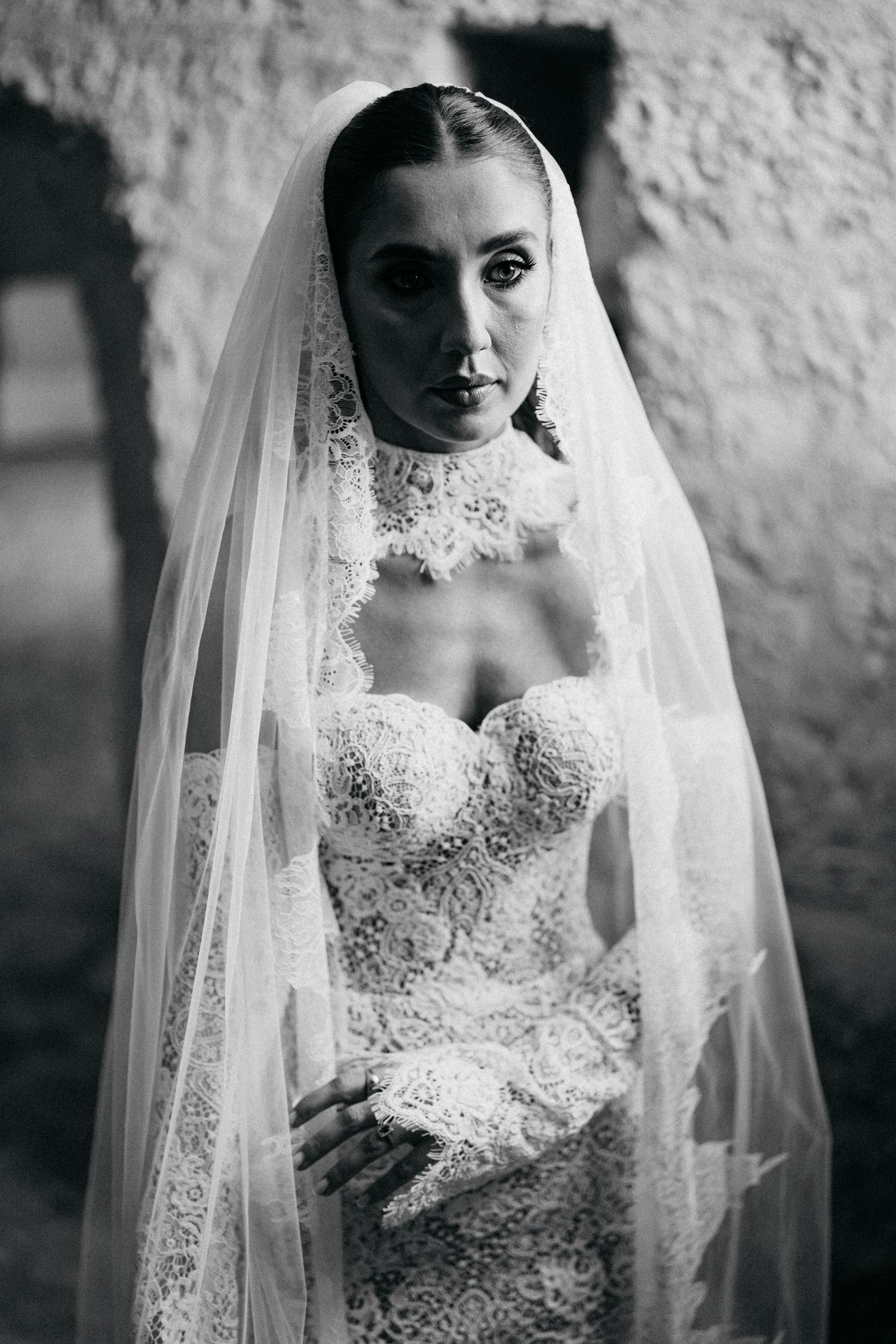 Black and white portrait of a bride in a strapless lace wedding gown with a sheer lace-trimmed veil and high collar.