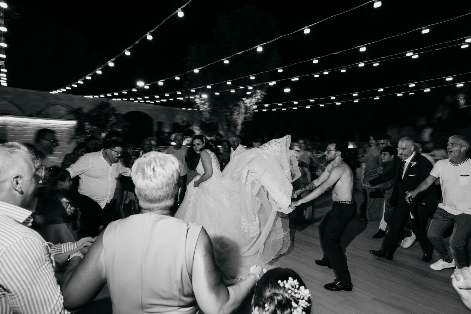 Black and white photo of wedding reception dance floor with string lights overhead.
