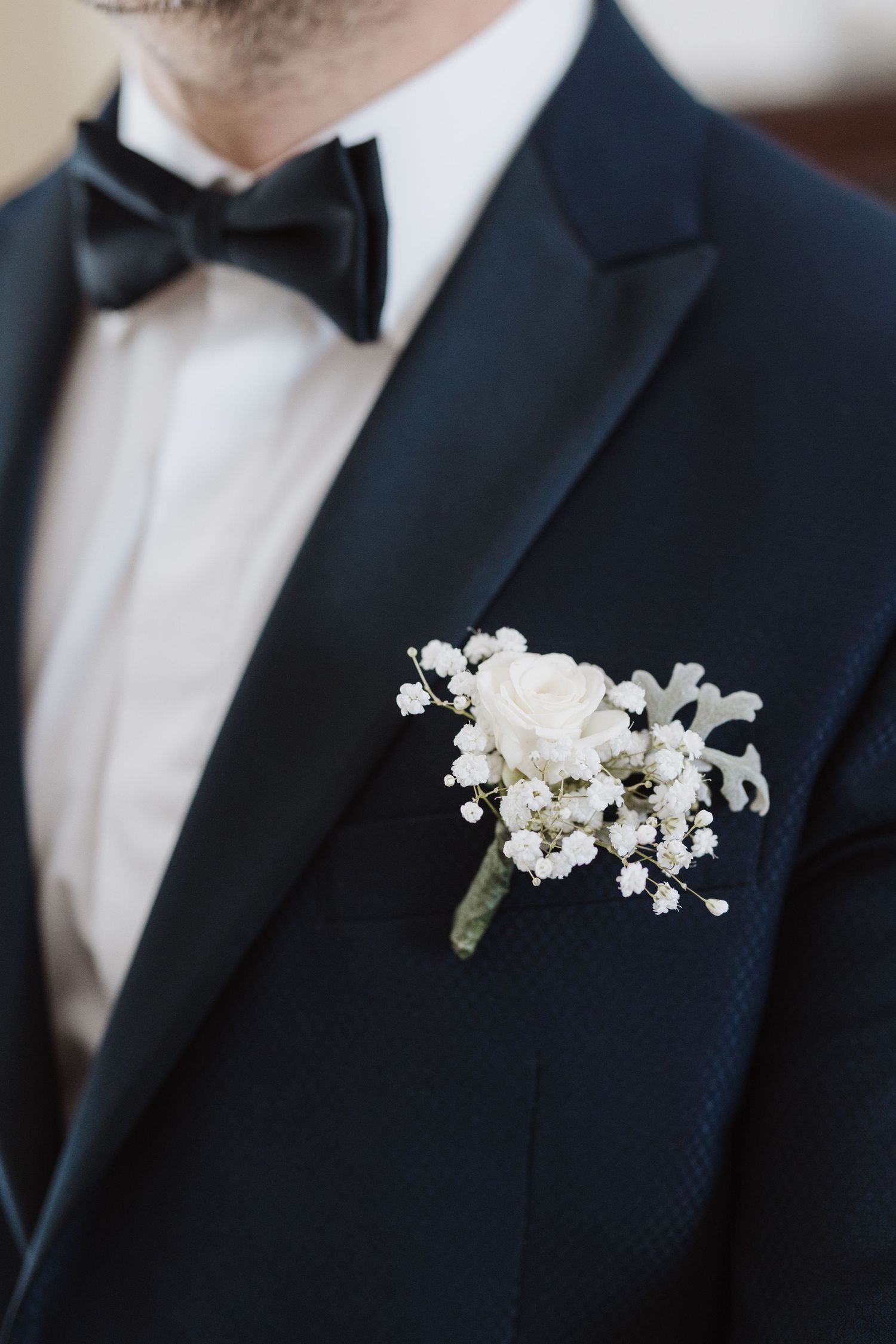 White floral boutonniere pinned to lapel of classic navy tuxedo with black bow tie.