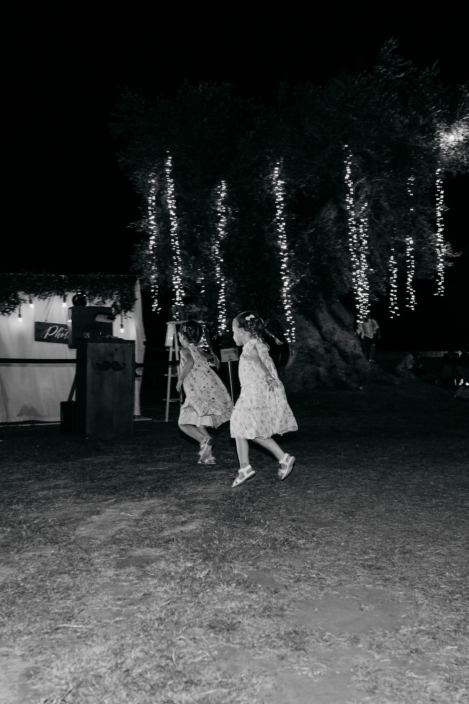 String lights illuminate an outdoor nighttime gathering in a garden setting.