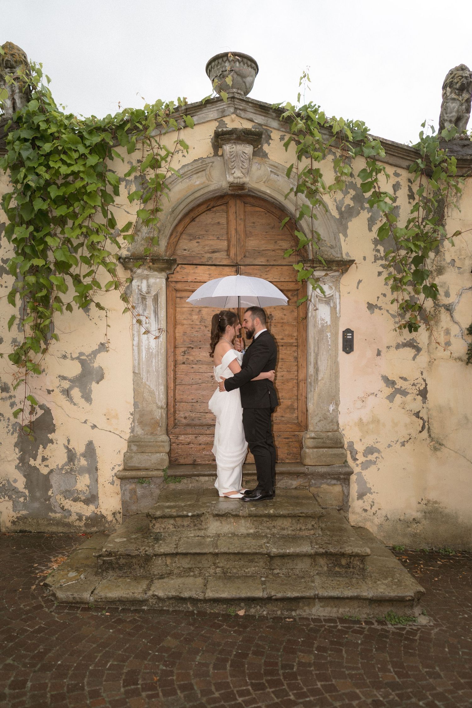 Wedding couple poses on stone steps in front of an ivy-covered historic building entrance.