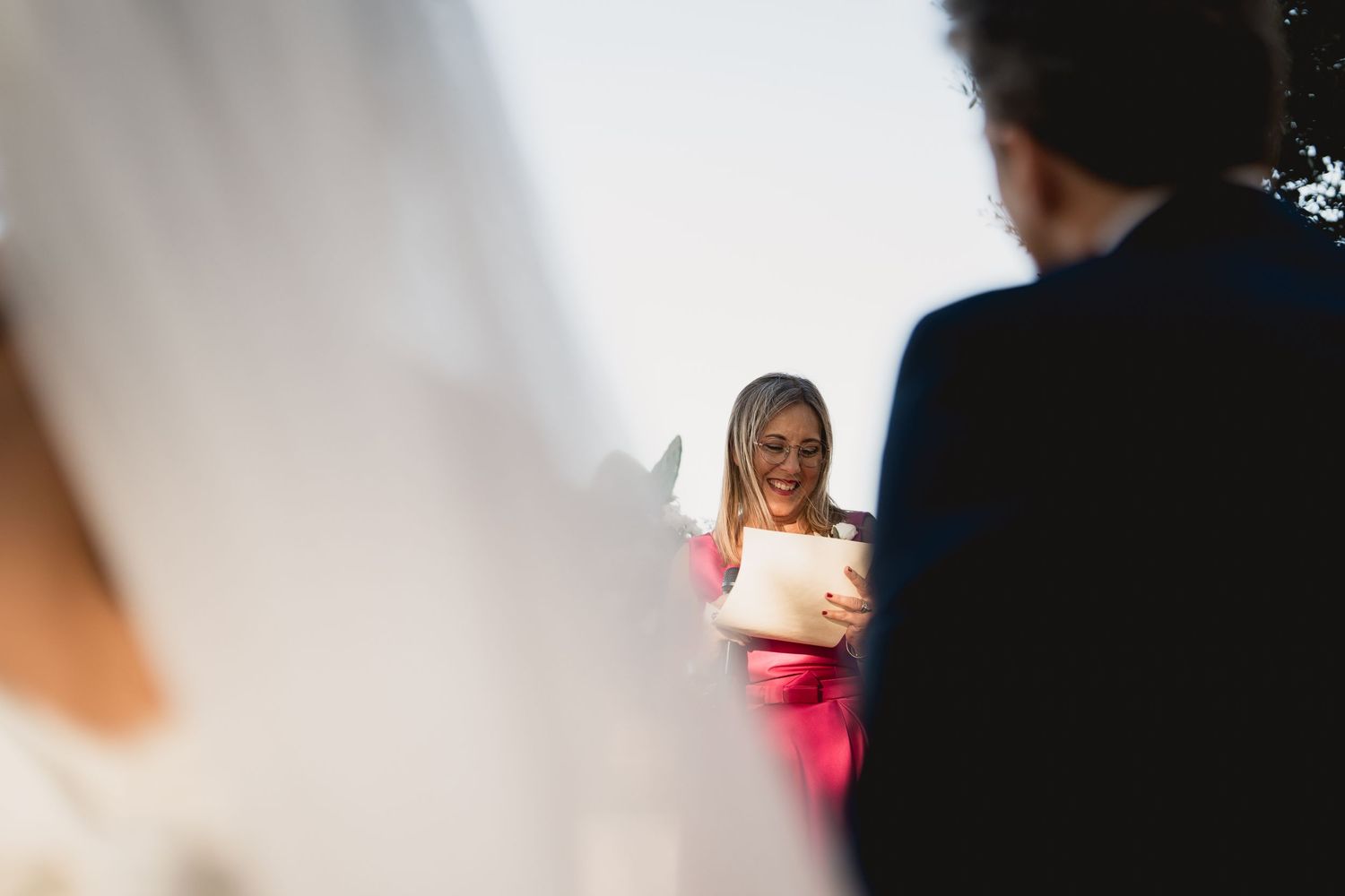 A guest reading during an outdoor wedding ceremony, captured through attendees.