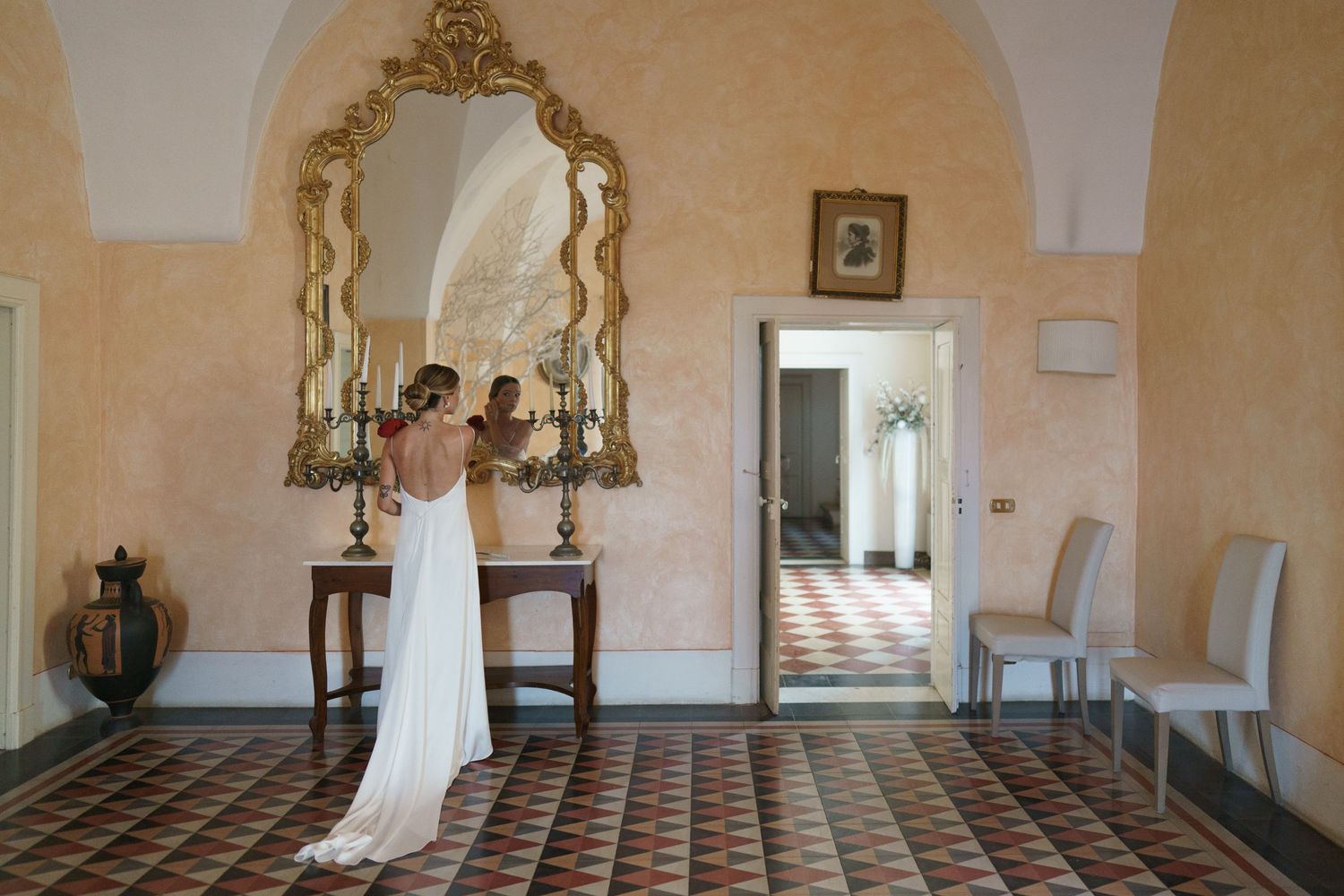 A romantic scene in a Mediterranean villa room with pink walls, ornate gold mirror, and tiled floors.