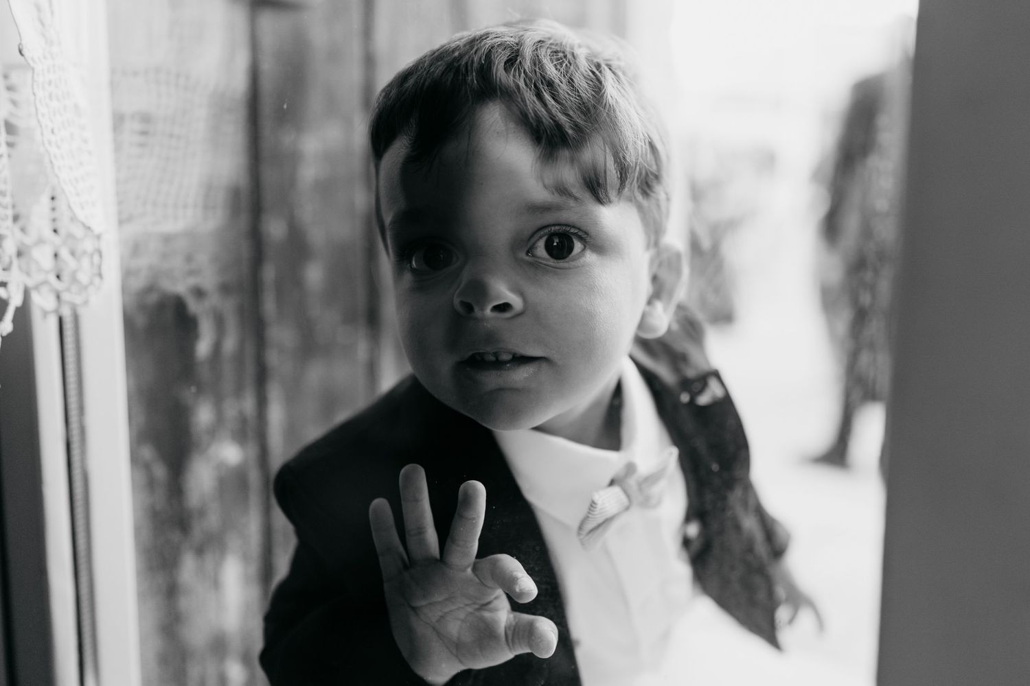 A black and white portrait of a young child looking through a window.
