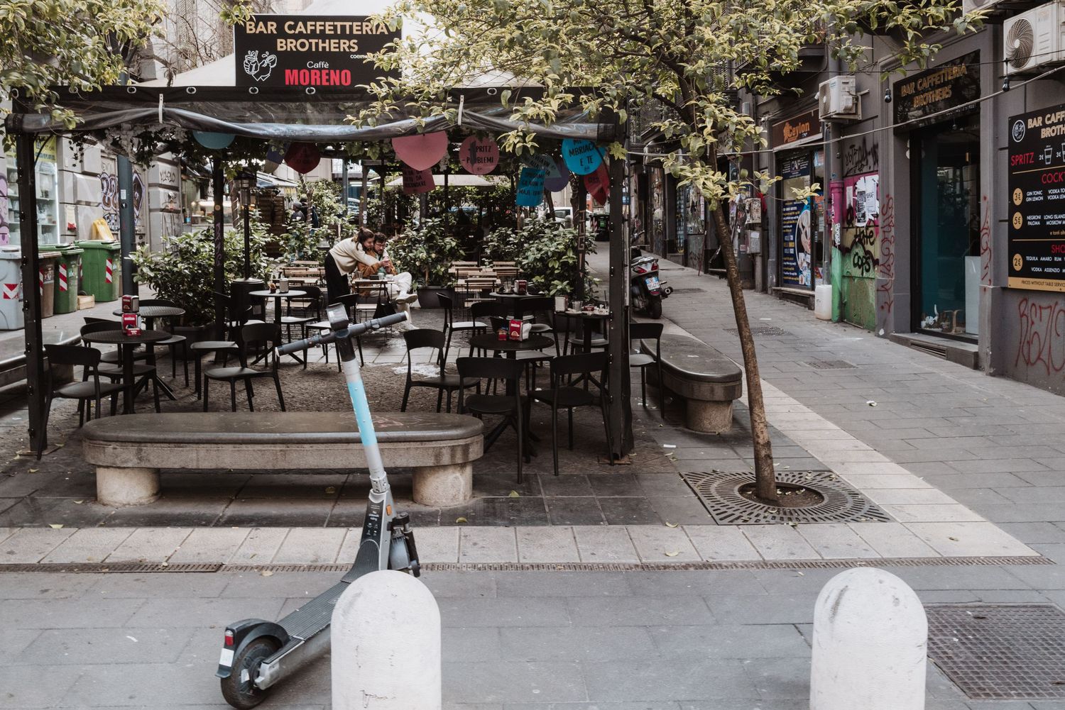 Empty outdoor cafe terrace with tables and chairs on a city street with an electric scooter parked in front.